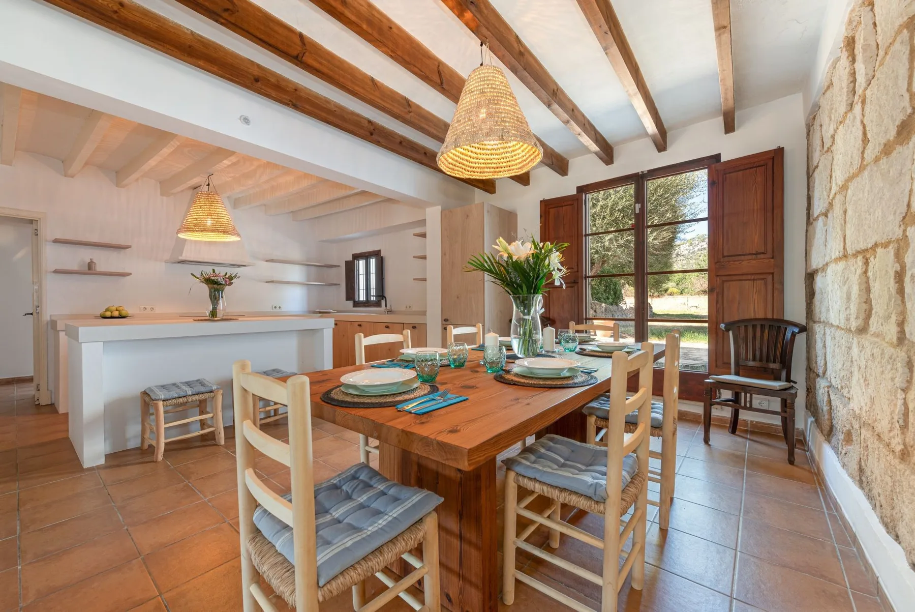 Comedor con una mesa de madera y sillas junto a ventanas abiertas.