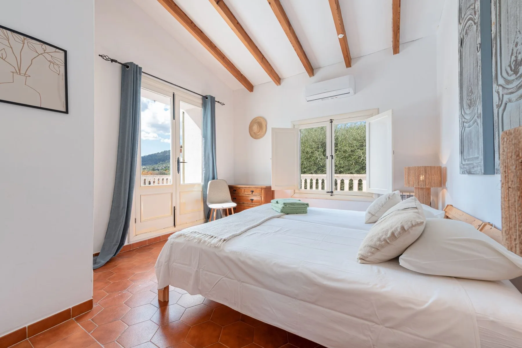 Un dormitorio luminoso con una cama grande, vigas vistas y ventanas abiertas.
