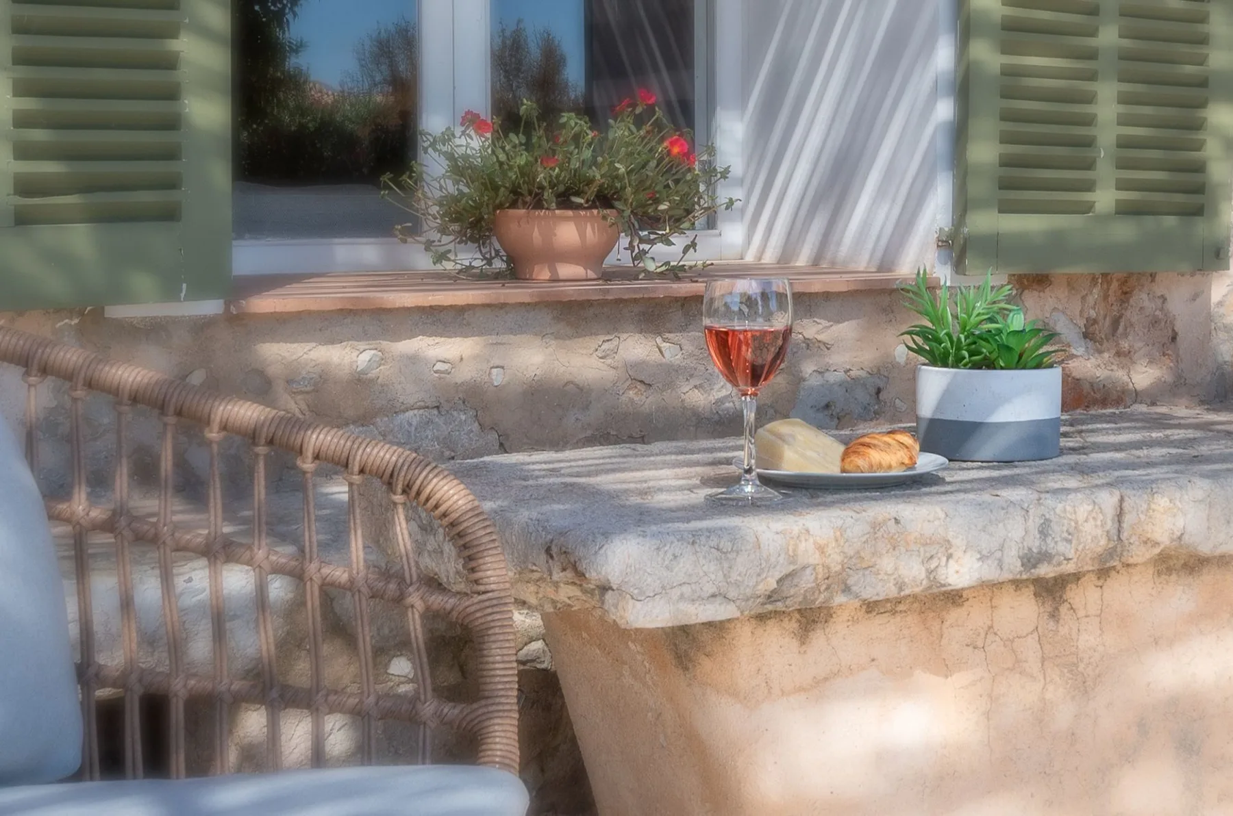 Una mesa de piedra en el patio sostiene una copa, un plato con comida y una planta en maceta.