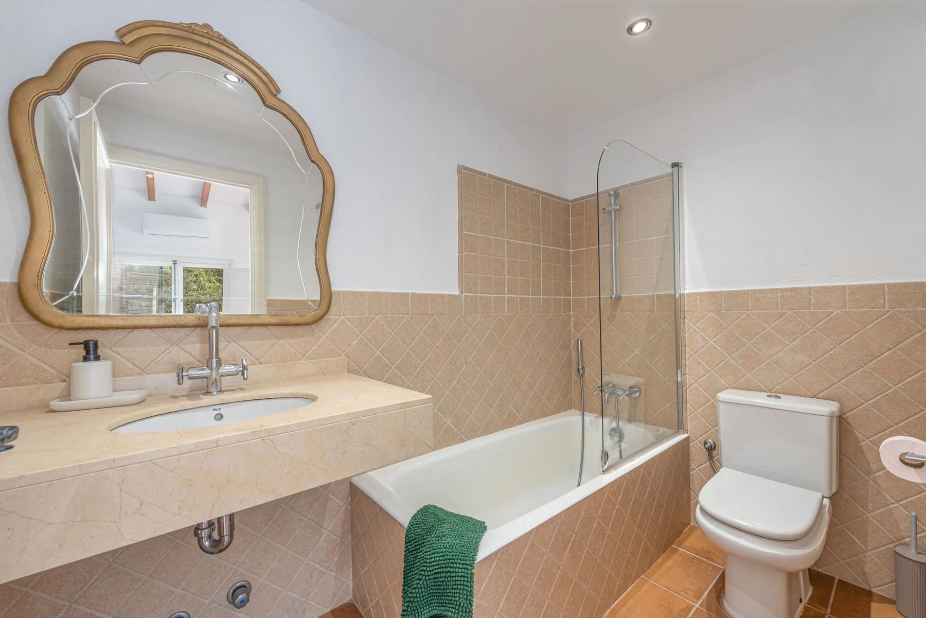 Un baño con azulejos, bañera, mampara de vidrio, lavabo e inodoro.