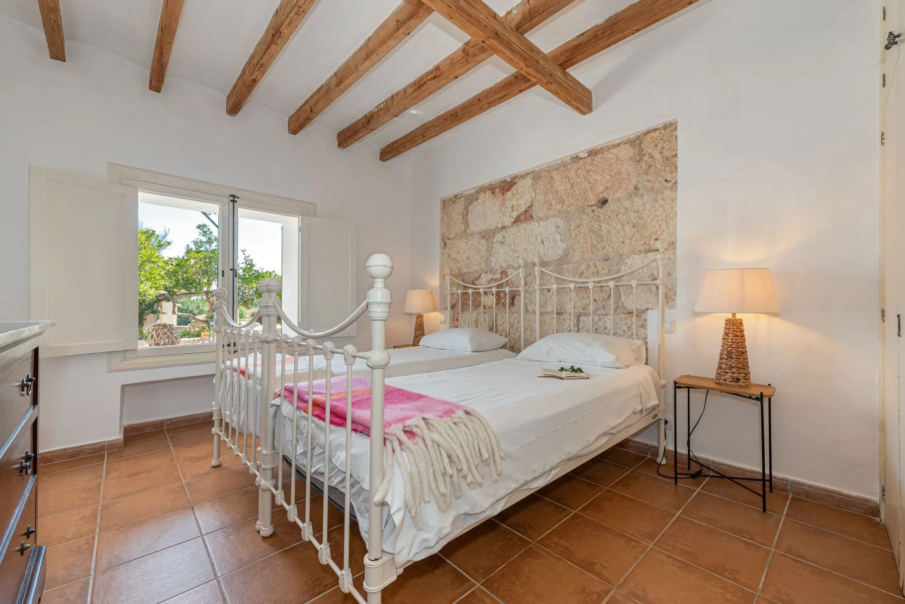 Un dormitorio con una cama blanca, lámparas de noche y vigas de madera expuestas.