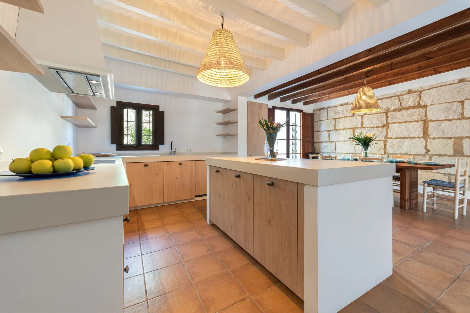 Una cocina luminosa con una gran isla central y una mesa junto a una pared de piedra.