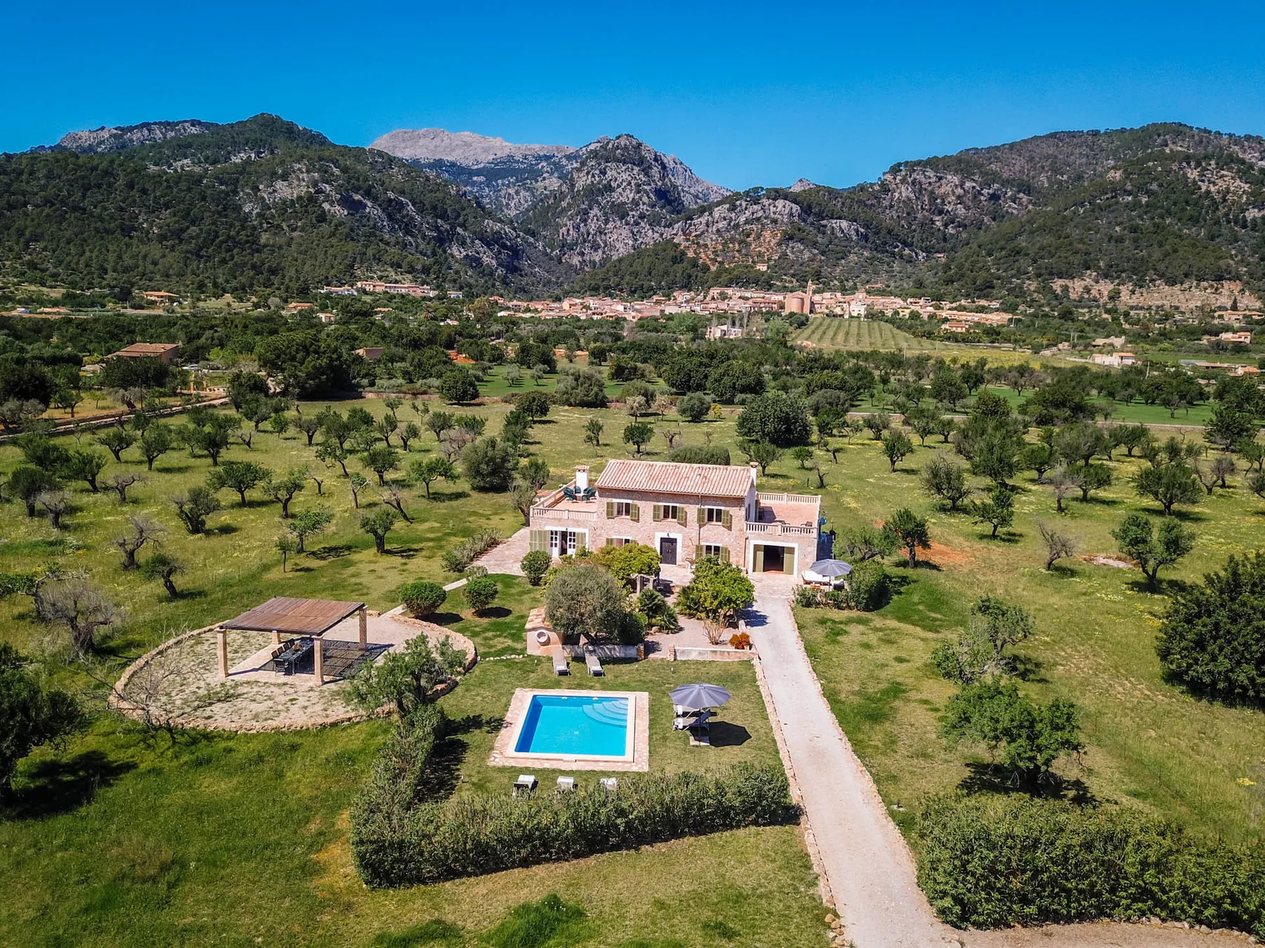 Una villa y una piscina están entre campos verdes, al pie de una cordillera.