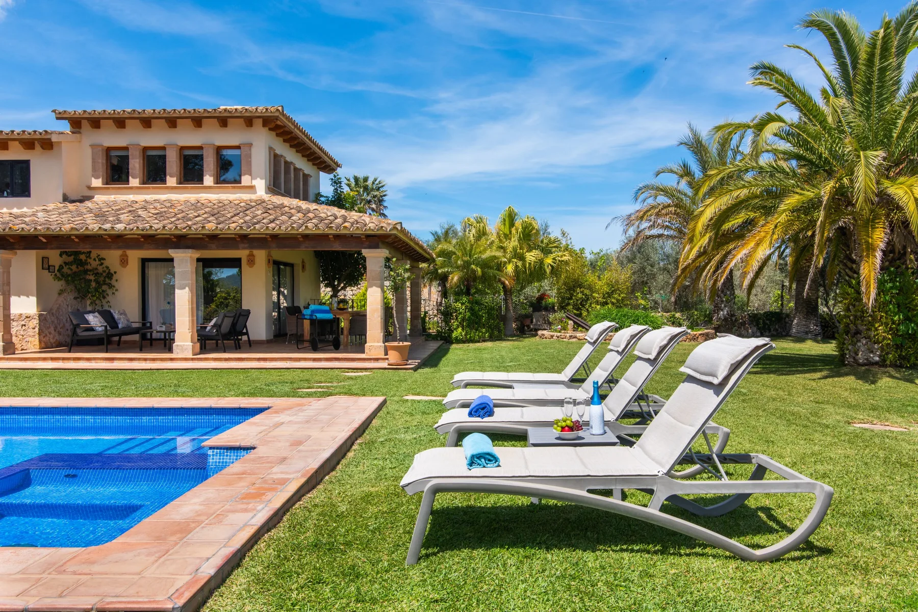 A swimming pool and lounge chairs sit beside a lawn and a house.