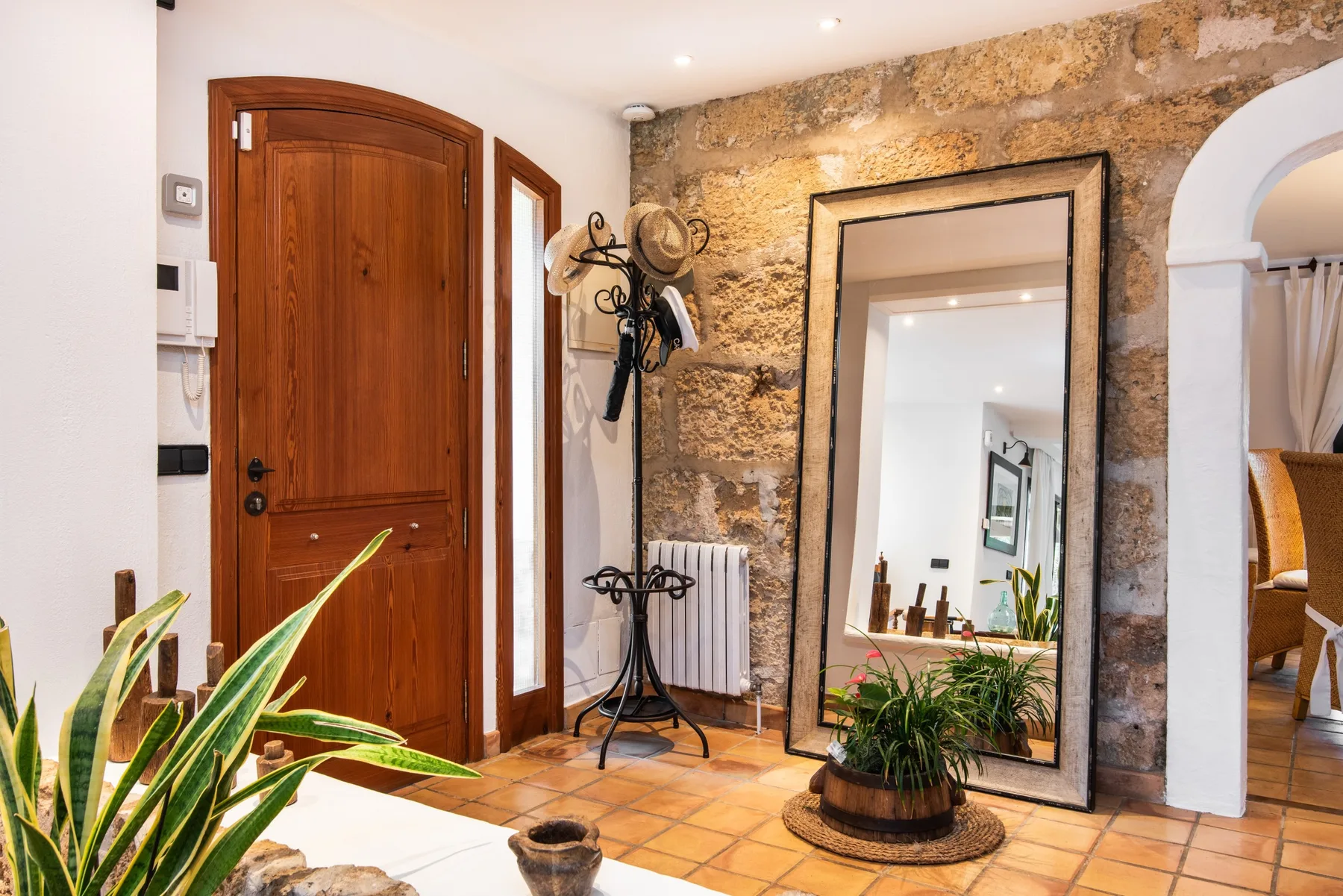 A stone entryway with a wooden door, a standing coat rack, and a large mirror.