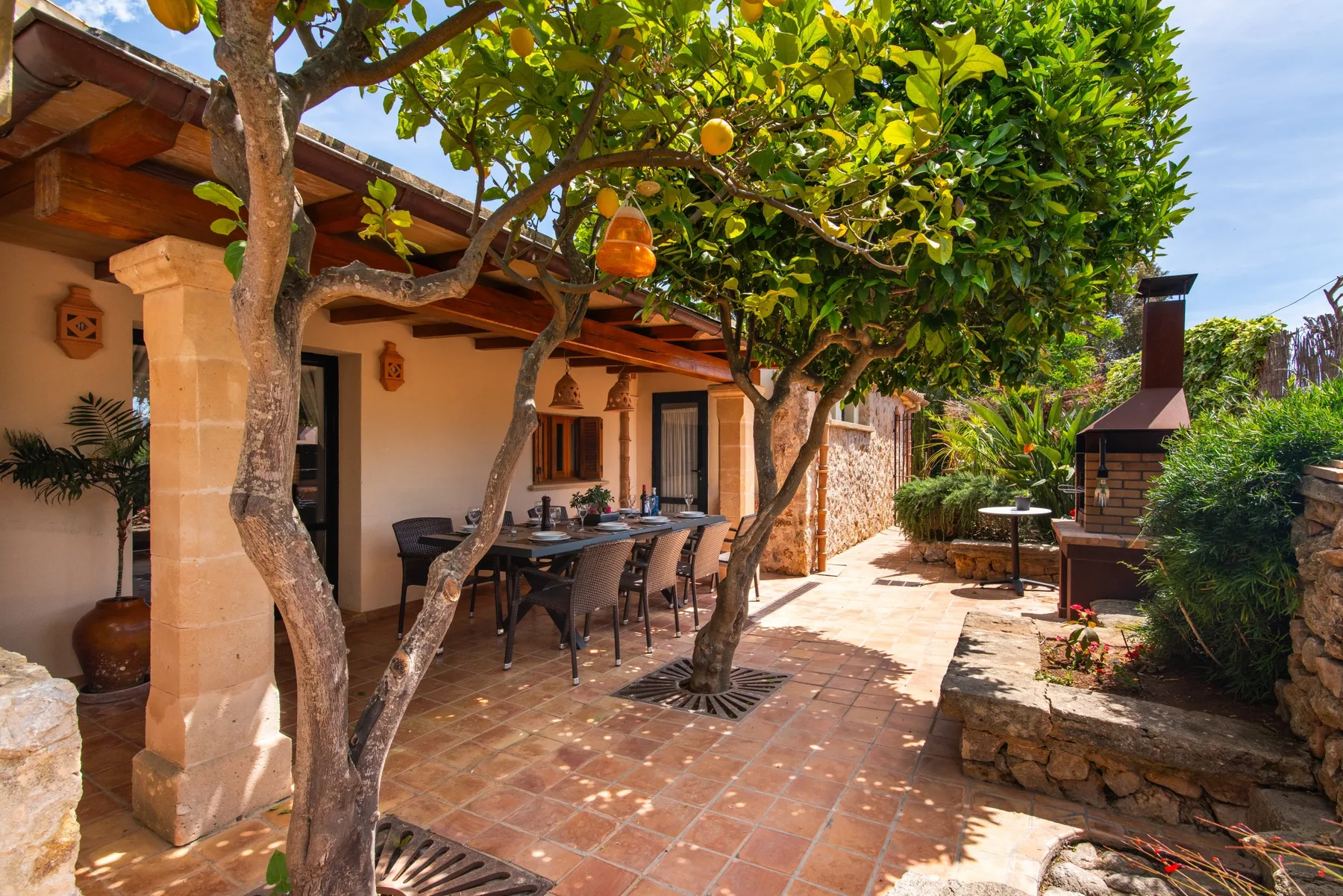 A shaded outdoor dining patio with a table beneath leafy trees.