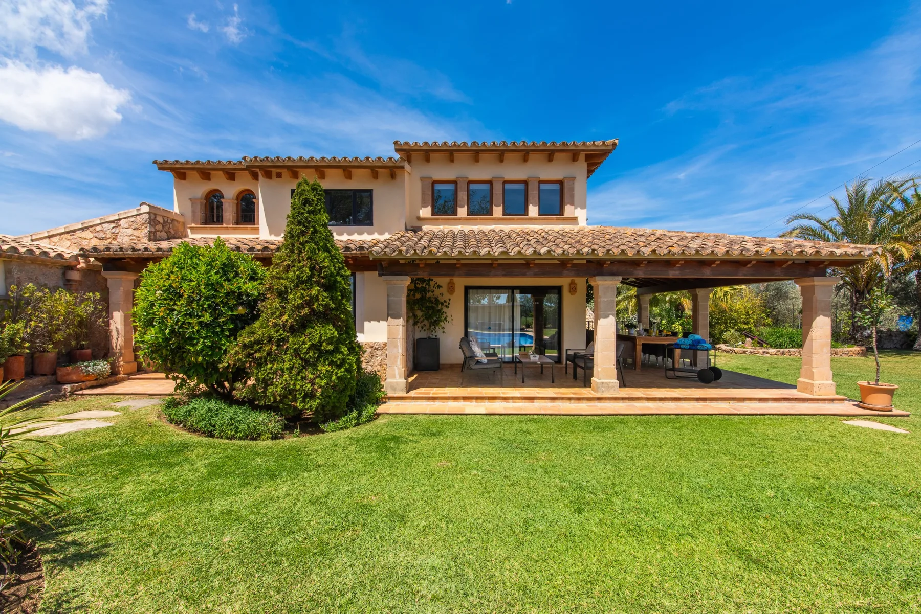 A two-story house with a covered patio overlooks a green lawn.