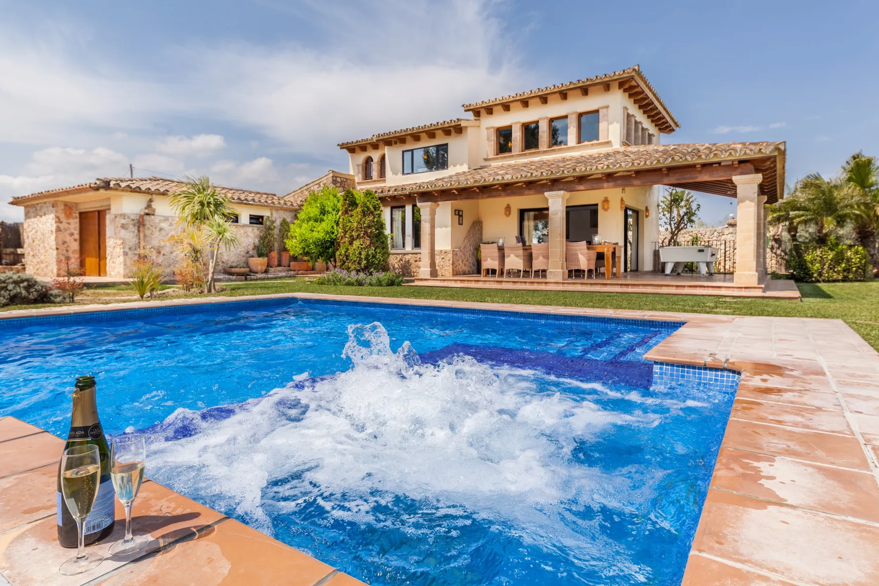 A swimming pool with bubbling water in front of a large house.