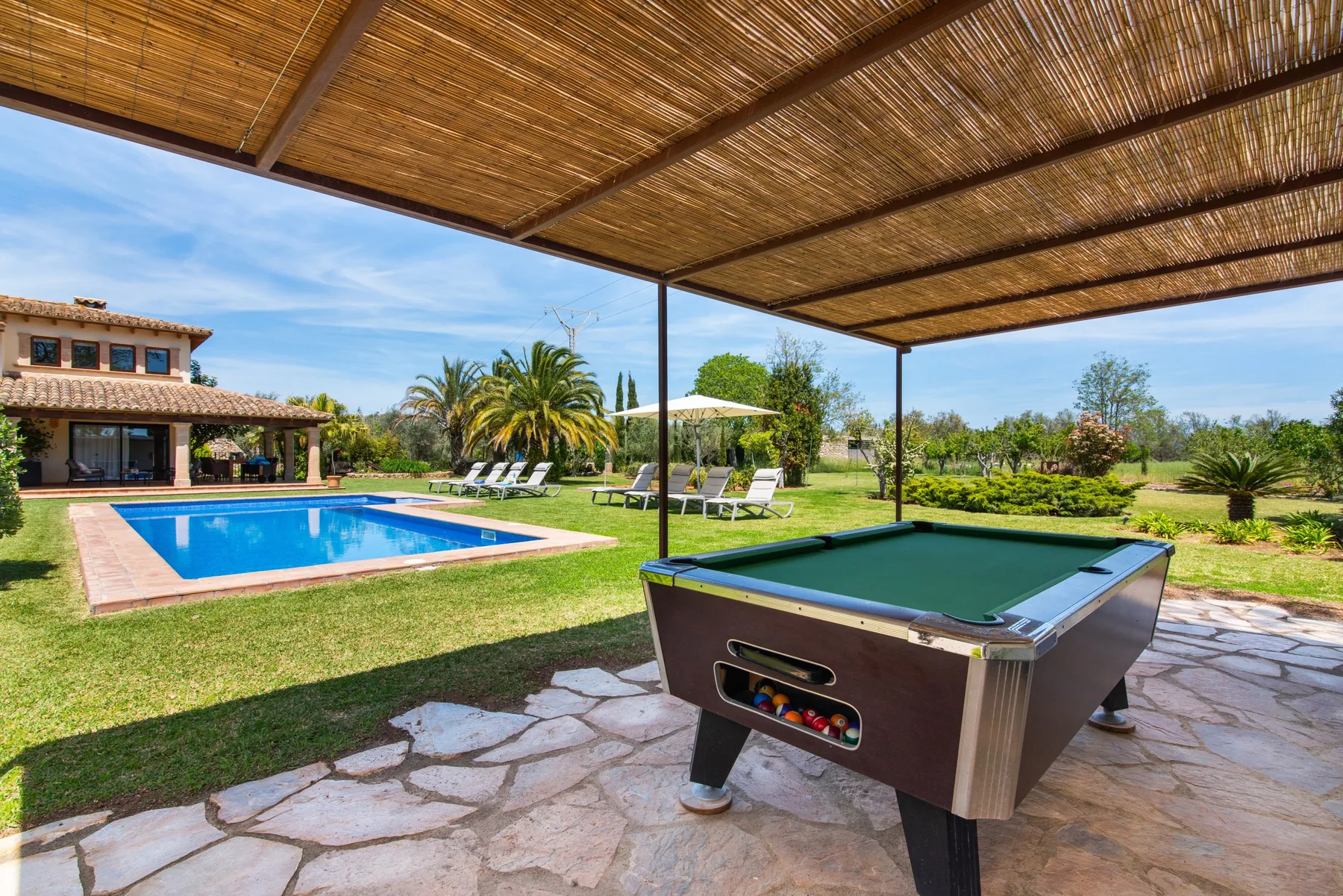A covered outdoor patio overlooks a swimming pool and a lawn with a game table.
