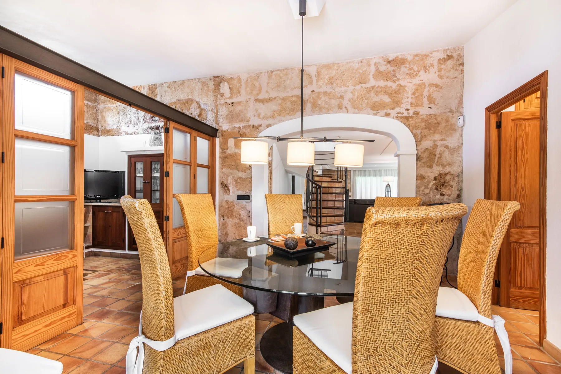 A dining area with woven seating around a glass table beneath pendant lights.