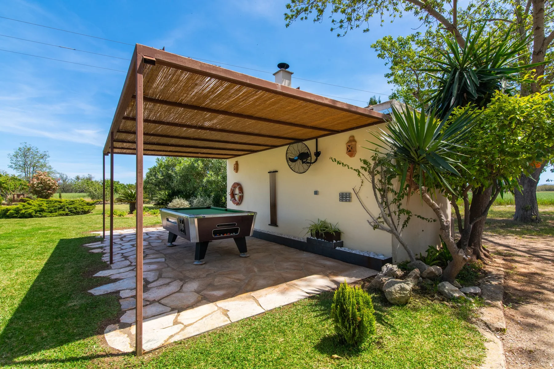 A covered outdoor patio with a pool table beside a garden.