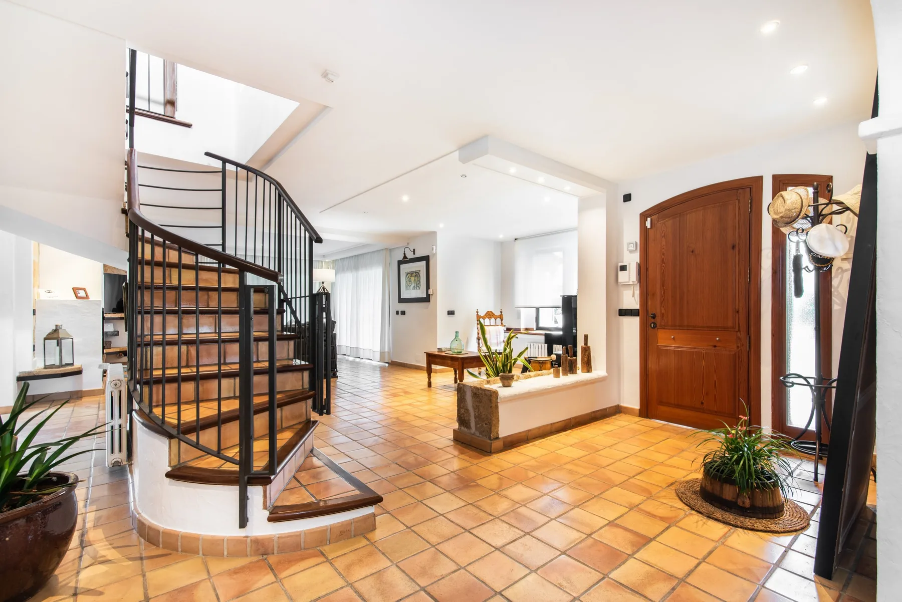 A bright tiled entryway features a curved staircase and a wooden front door.