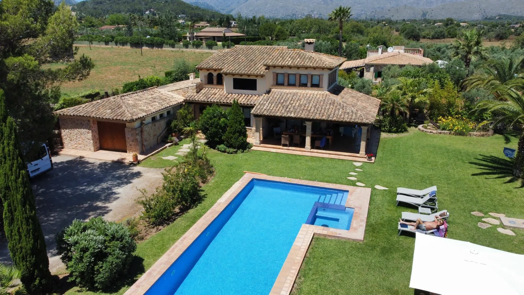A large house overlooks a swimming pool, lawn, and landscaped grounds.