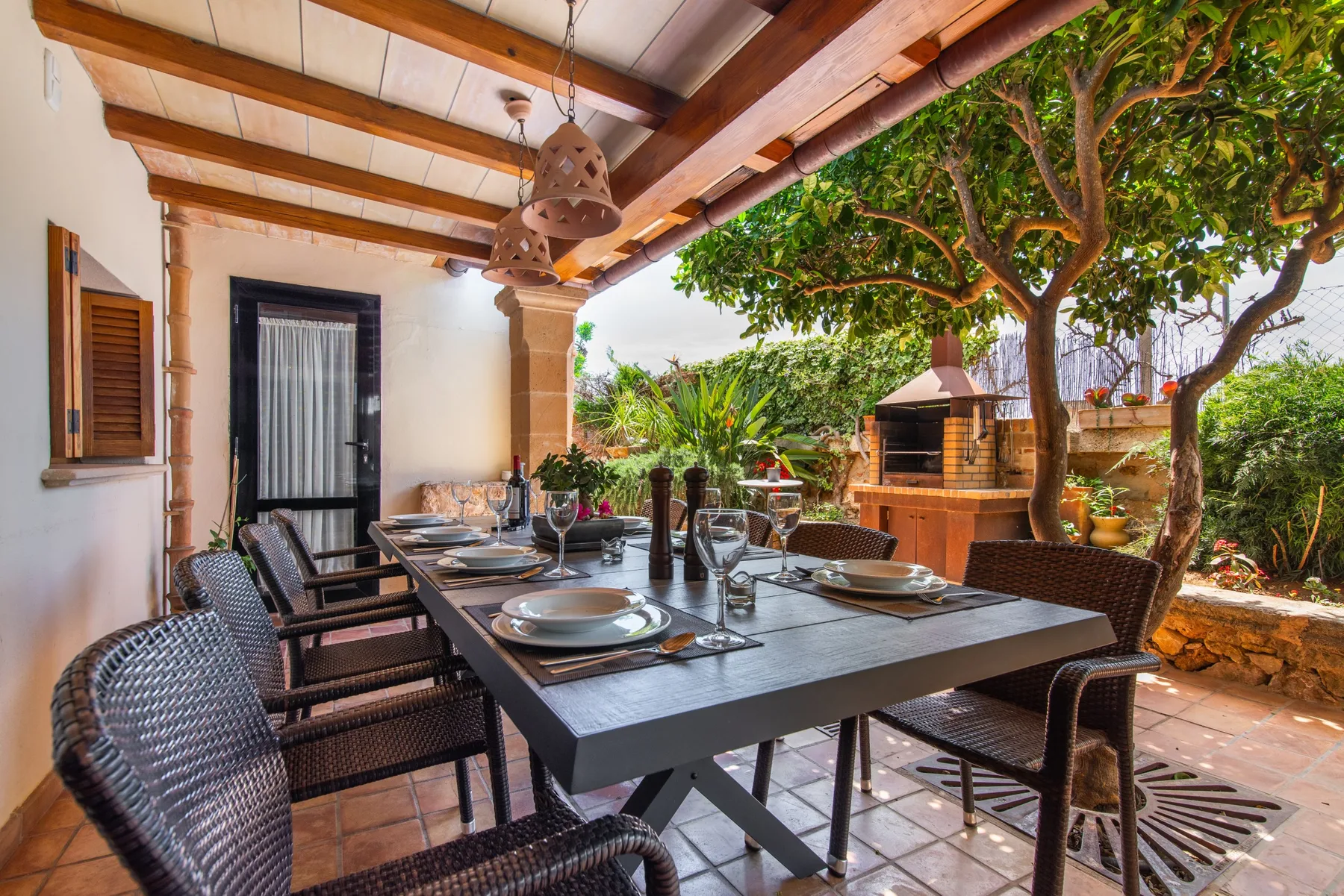 A covered outdoor dining area with a set table and leafy garden.