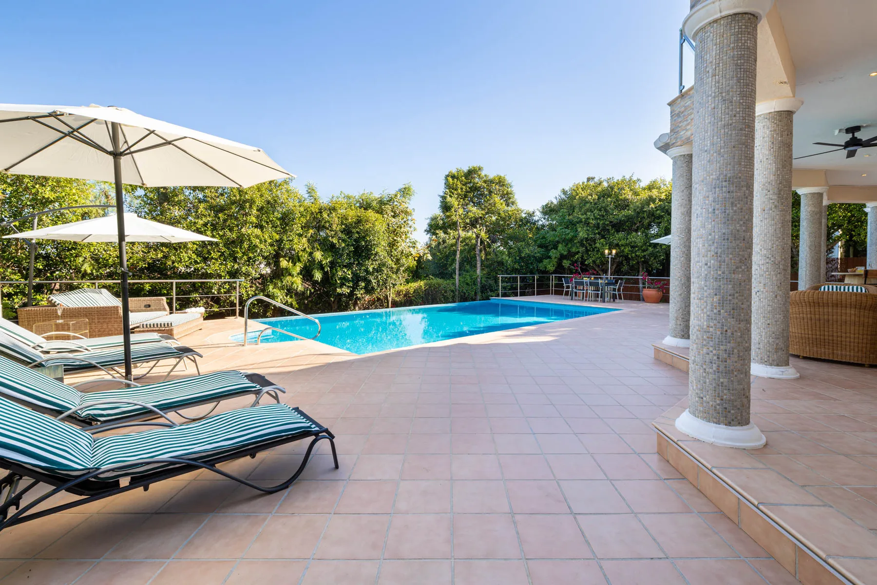 An outdoor pool beside a tiled patio with lounge seating and umbrellas.