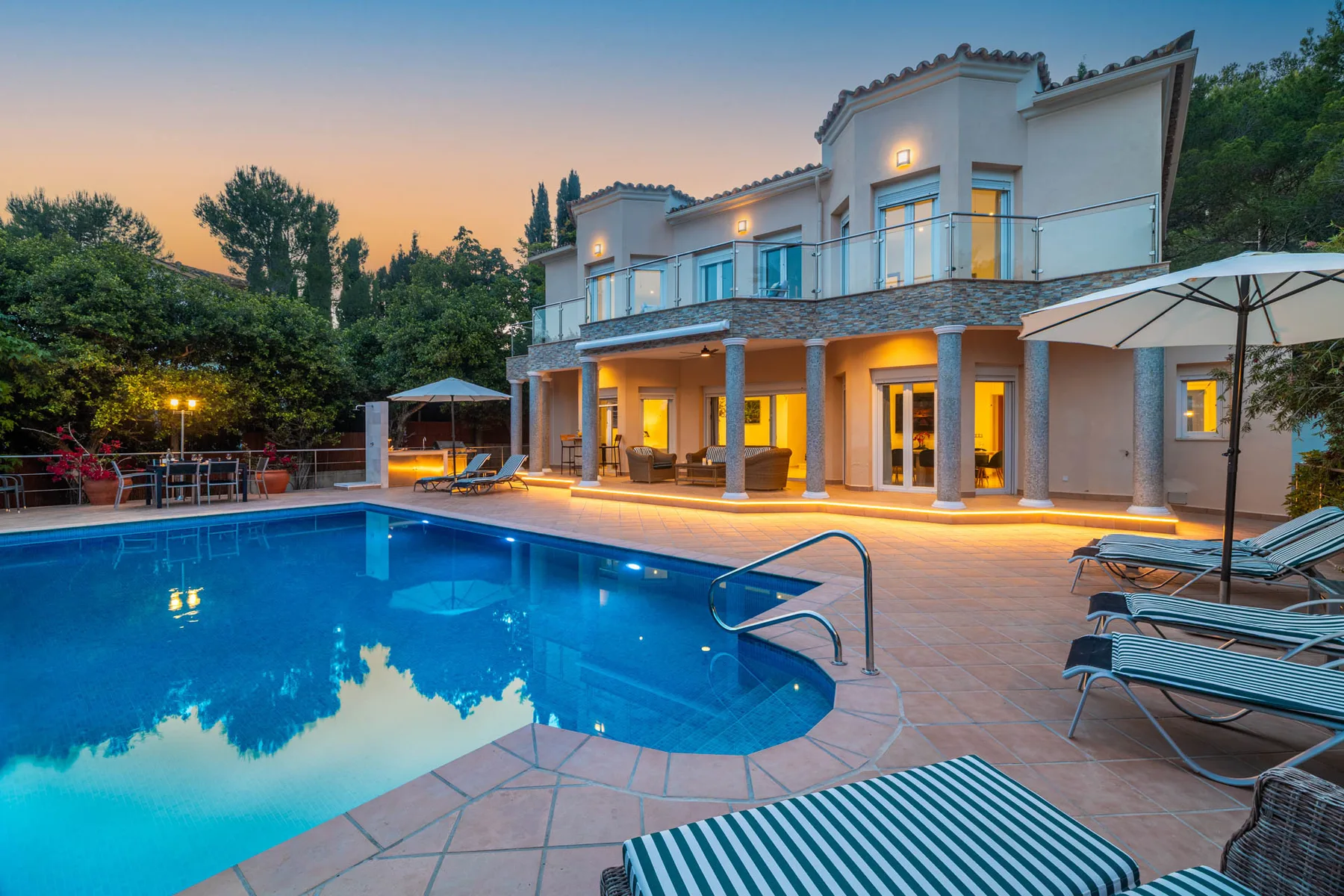 A modern house overlooks a swimming pool with lounge seating at dusk.