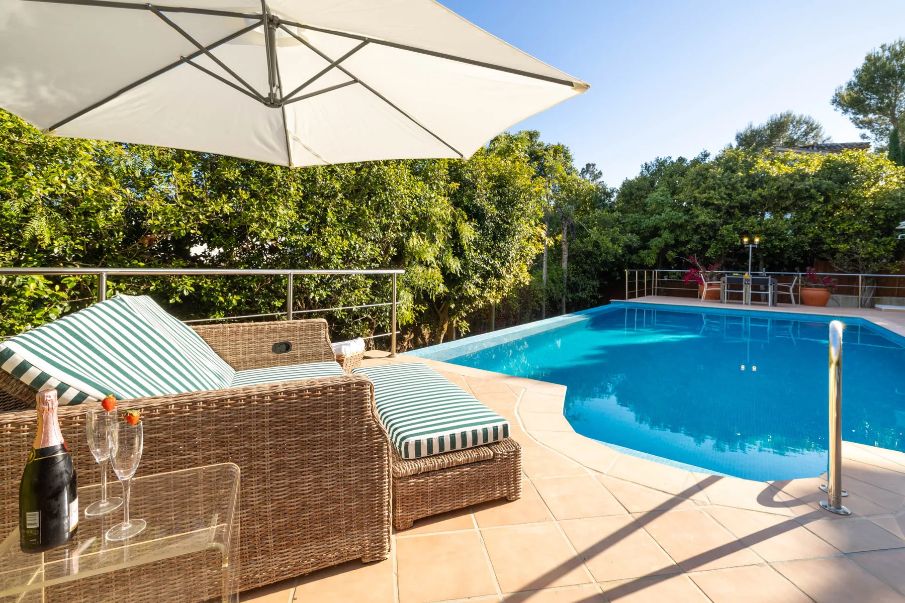 An outdoor swimming pool beside a shaded seating area and leafy greenery.