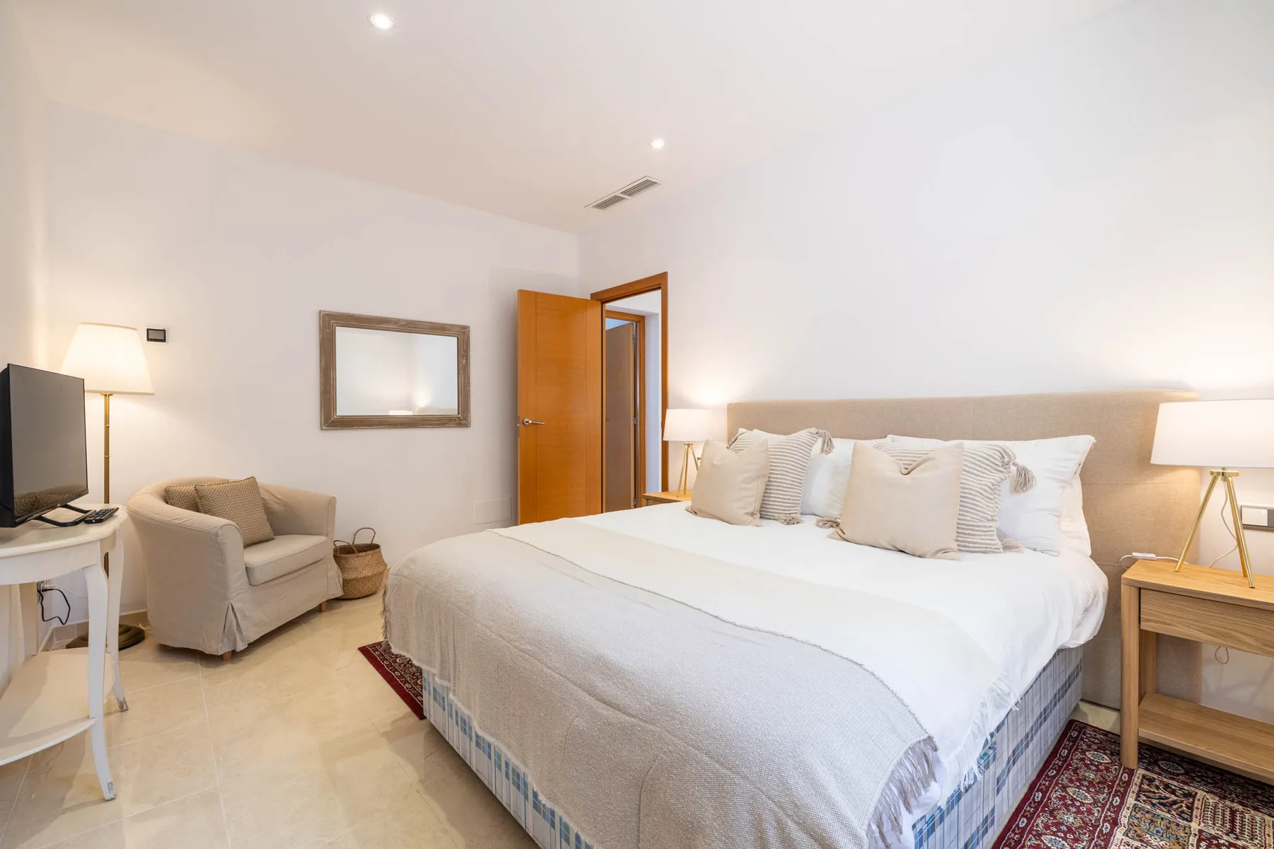 A bright bedroom with a large bed, bedside tables, and a small seating area.