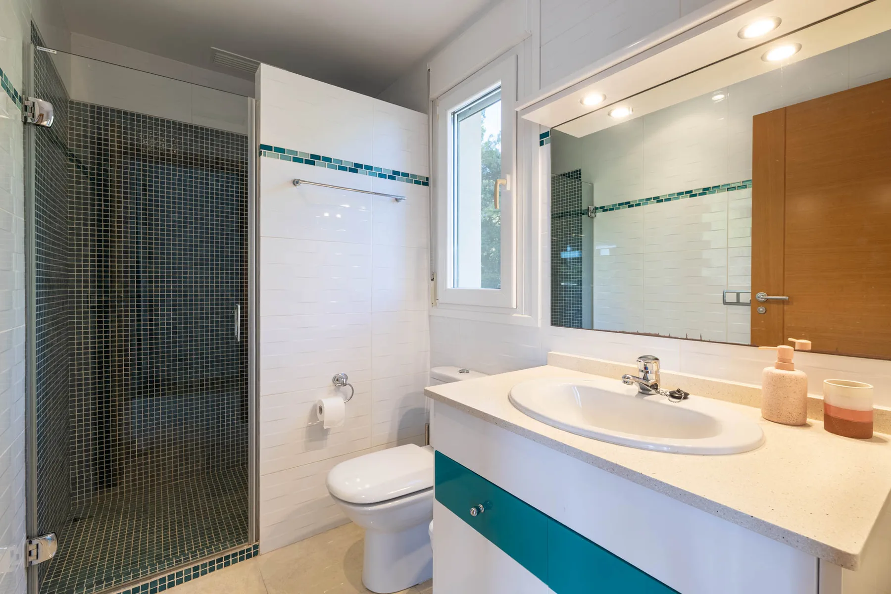 A bathroom with a glass shower, toilet, and a vanity beneath a large mirror.
