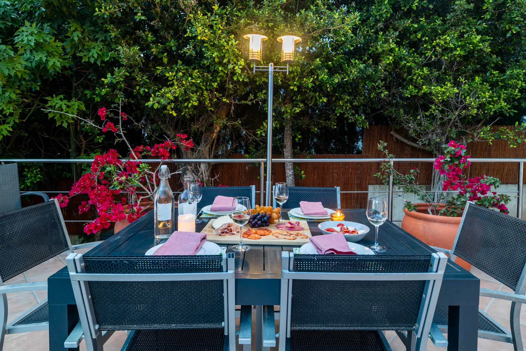An outdoor dining area has a set table surrounded by greenery.
