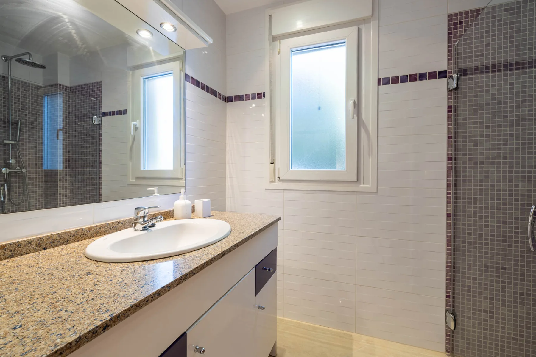 A bright bathroom with a sink, mirror, and tiled shower area.