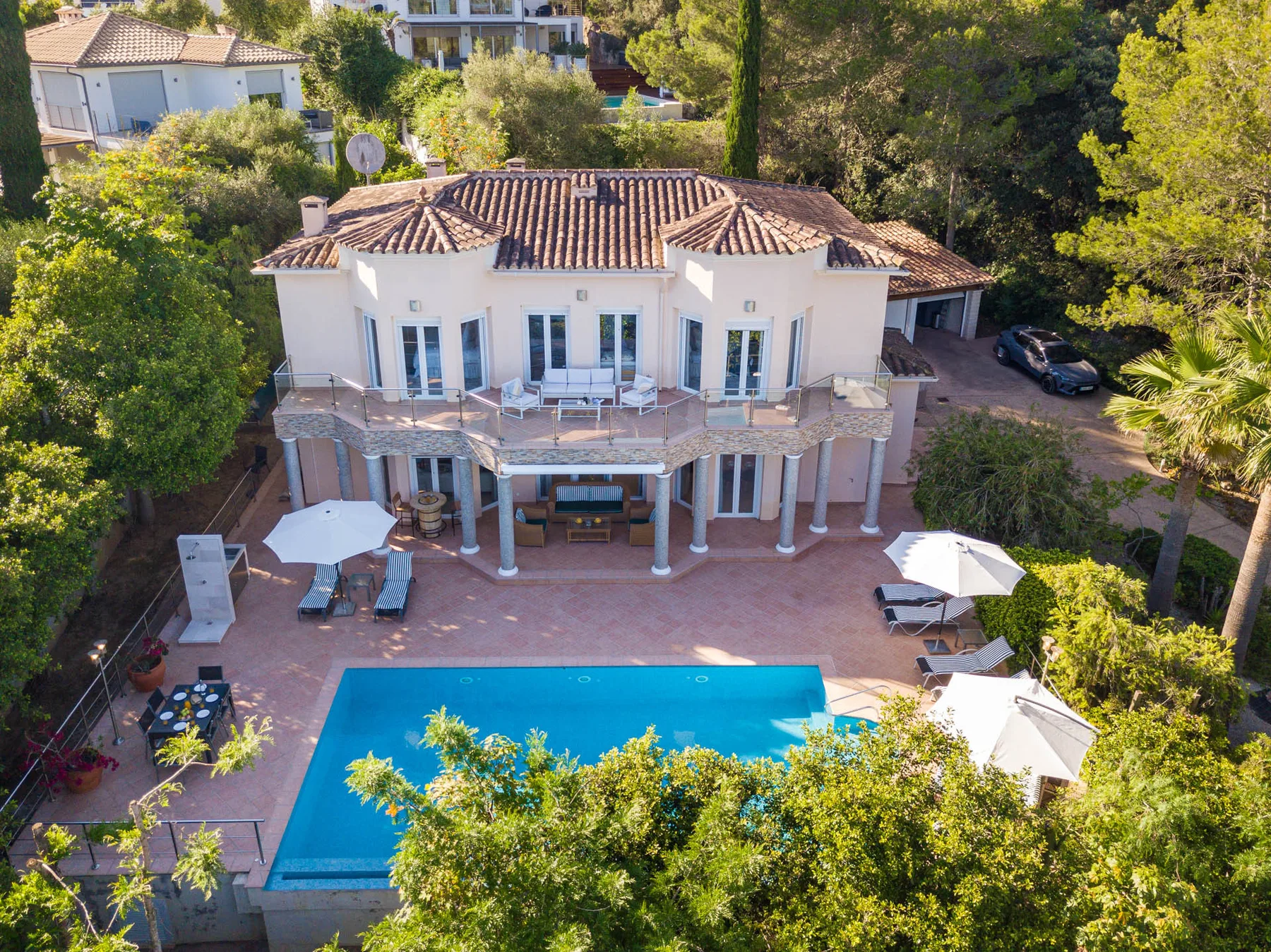A large house overlooks a swimming pool and paved outdoor seating area.