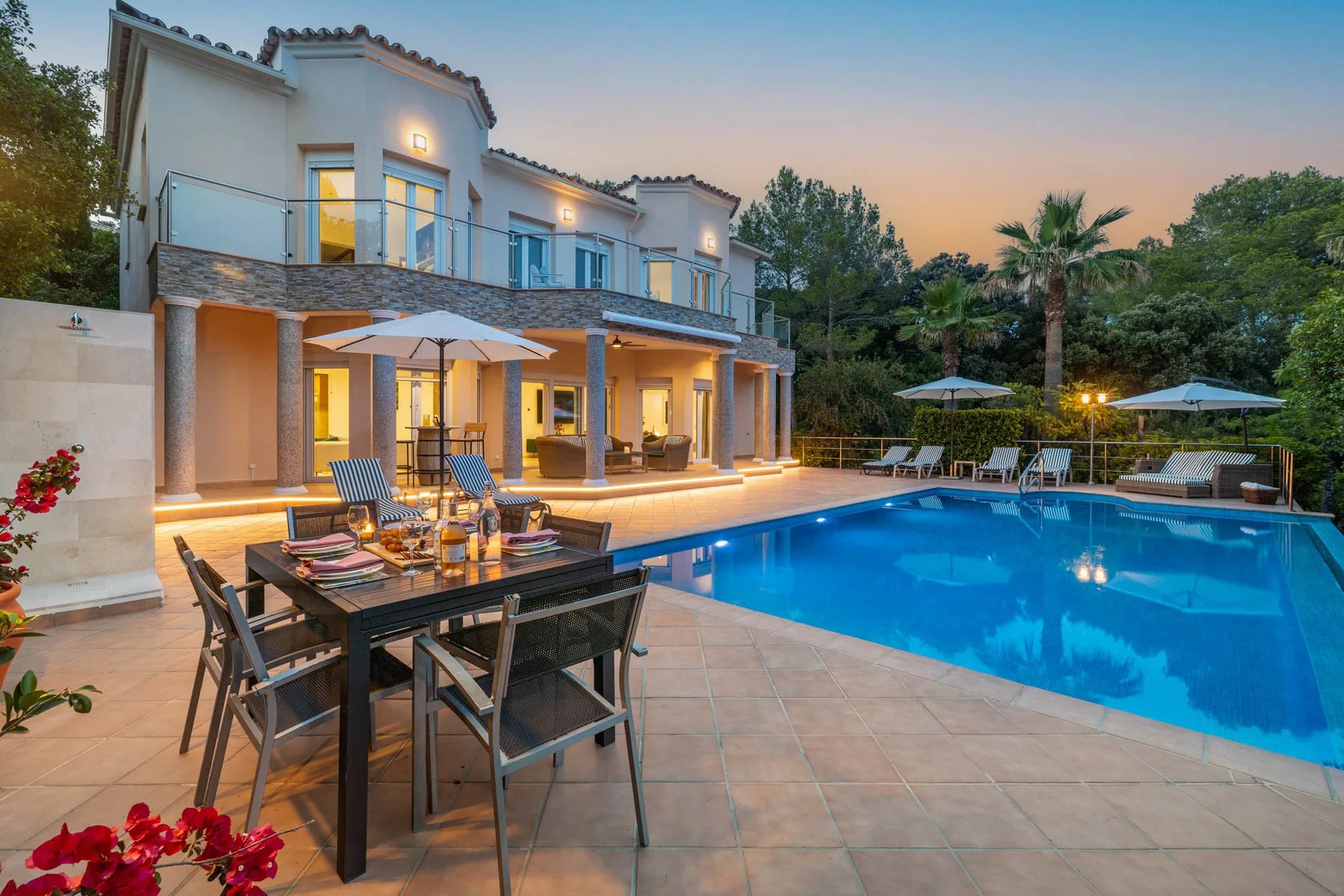 A villa patio overlooks a swimming pool, with outdoor dining seating beside the water.