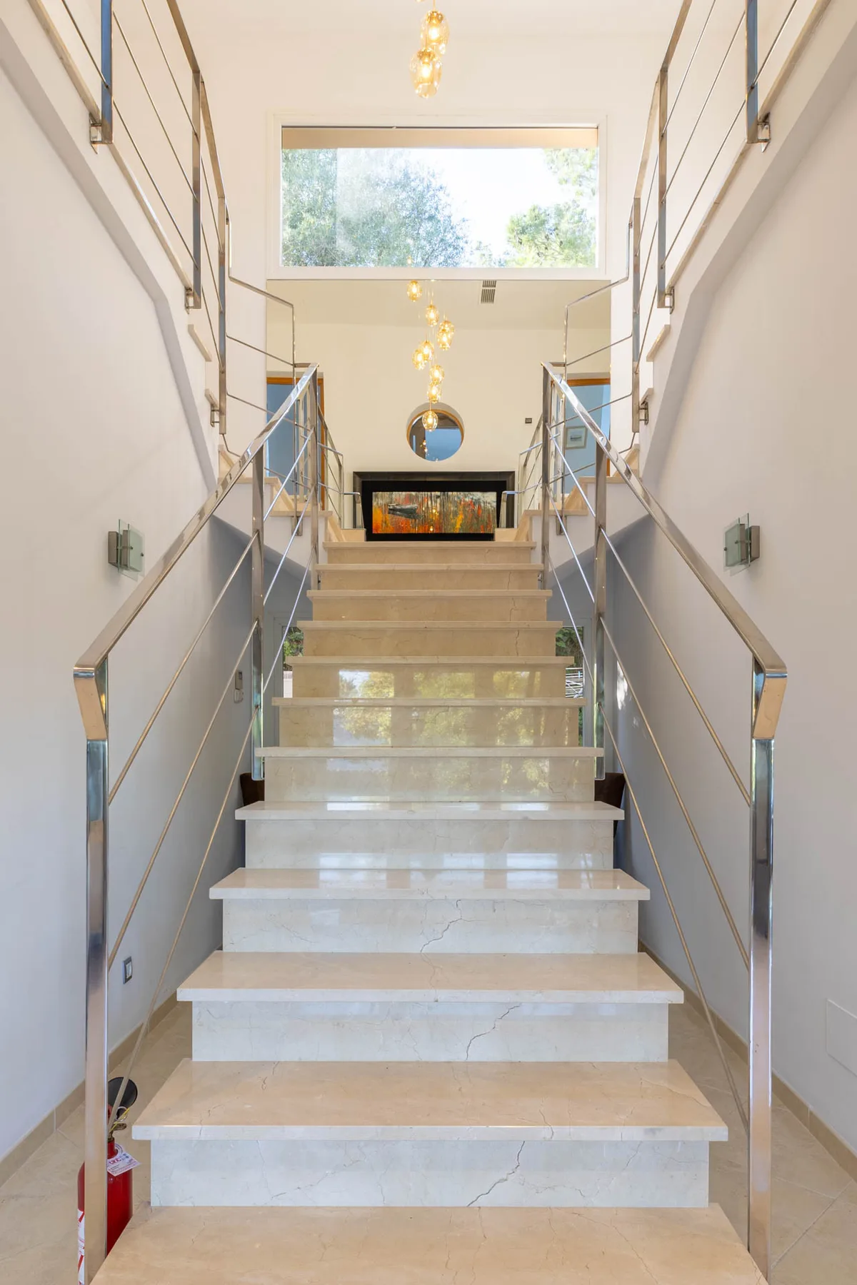 A bright interior staircase with metal handrails and a large window above the landing.