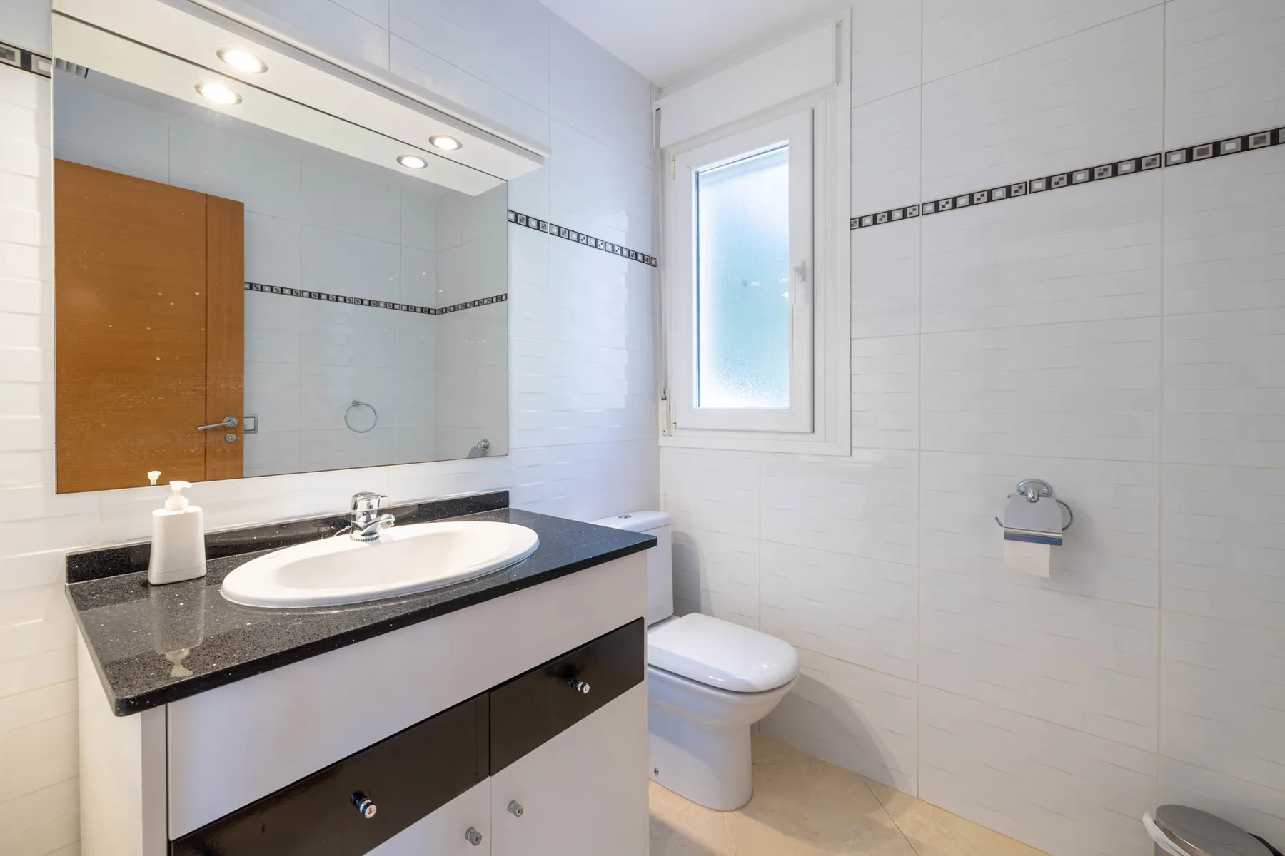 A bright tiled bathroom with a sink vanity and a frosted-glass window.