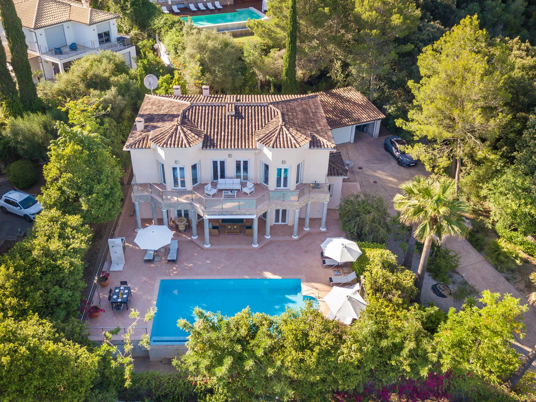 An aerial view of a large house beside a swimming pool, surrounded by trees.