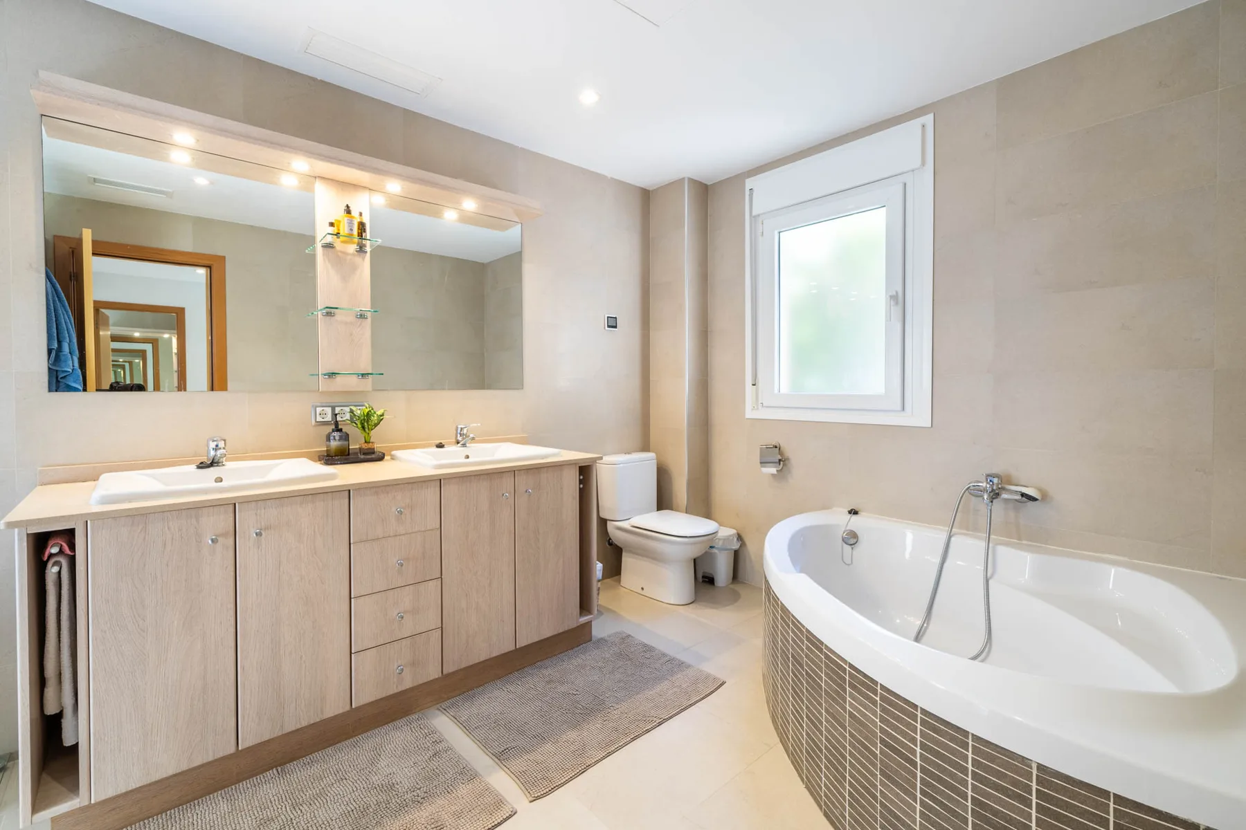 A bright bathroom with a long vanity, large mirror, and bathtub.