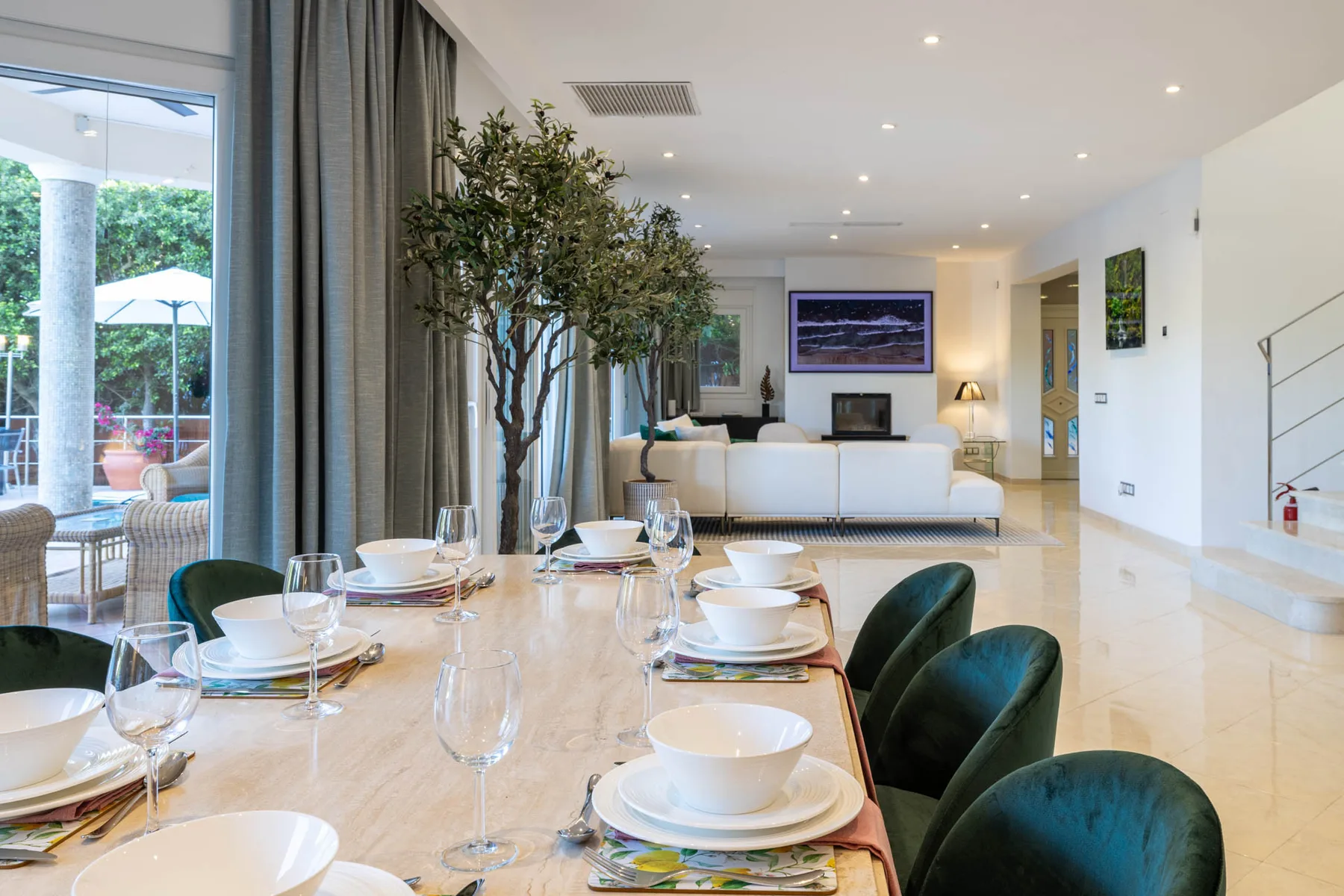 A dining table set with dishes overlooks a bright living room.