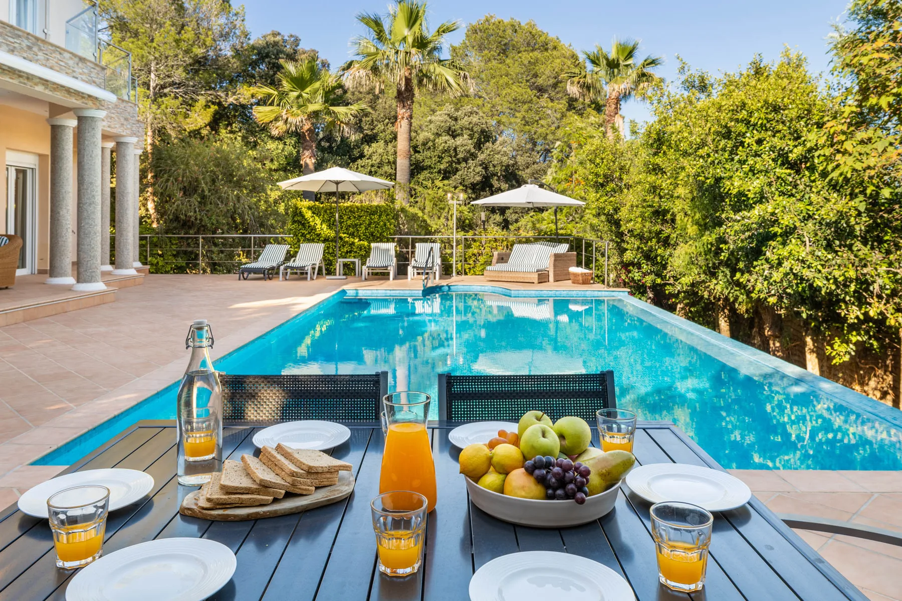 An outdoor swimming pool beside a patio, with a table set with food and drinks.