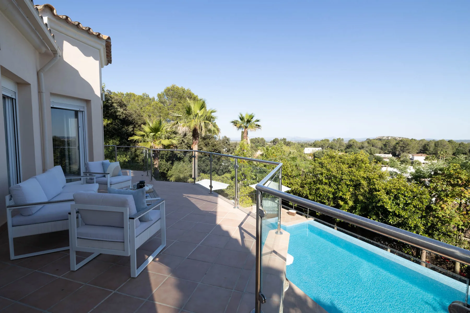 A terrace with outdoor seating overlooks a swimming pool and green landscape.