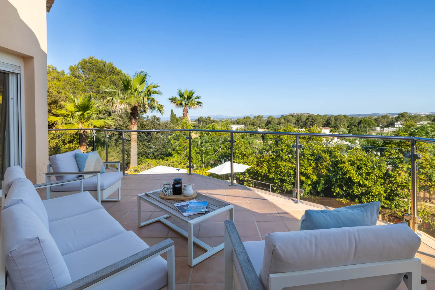 An outdoor terrace with cushioned seating and a glass railing overlooking trees.