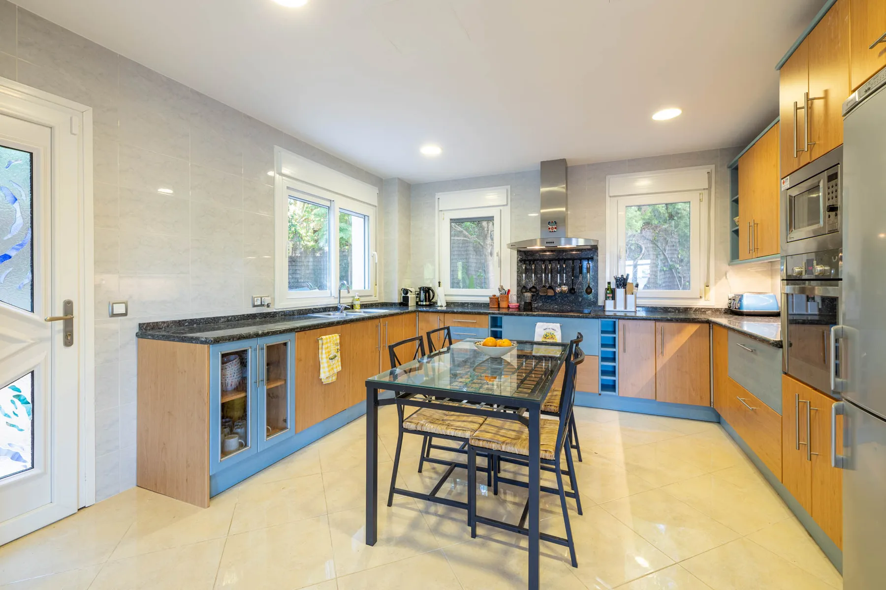 A bright kitchen with wood cabinetry, pale countertops, and a central dining table.
