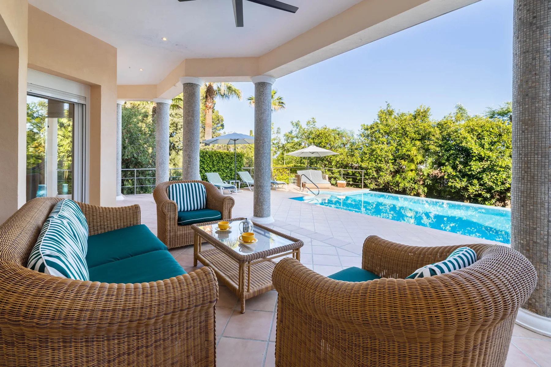 A covered outdoor seating area overlooks a swimming pool and garden.