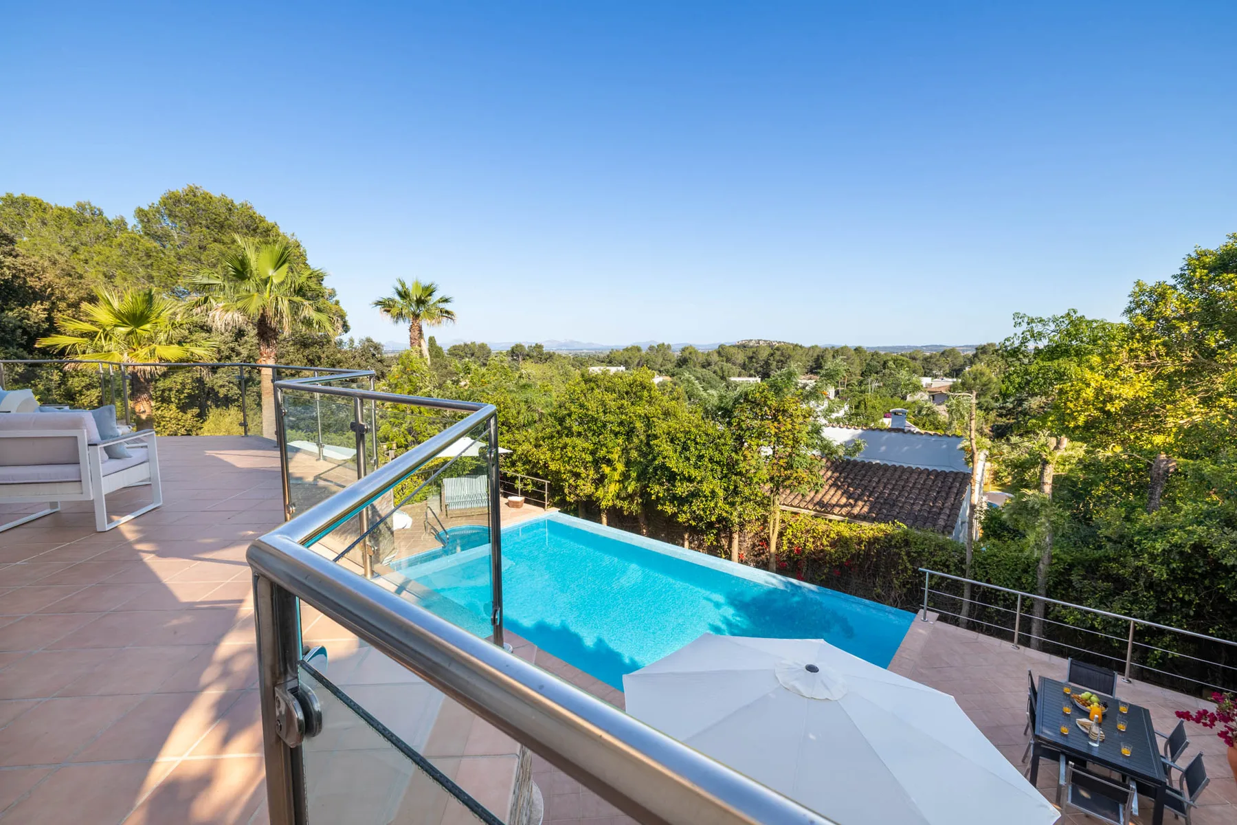 An outdoor swimming pool overlooks leafy trees and a distant landscape.