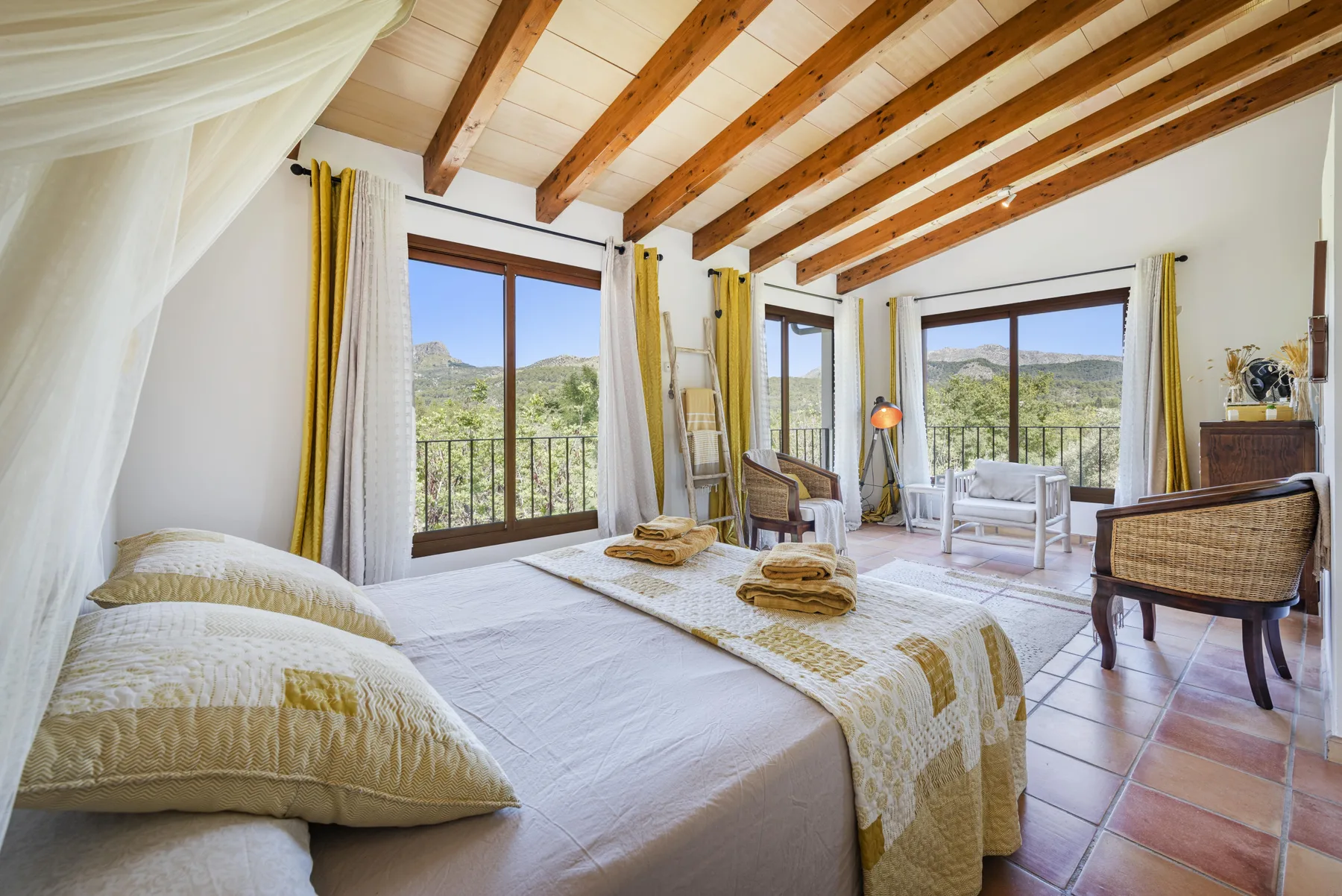 Un dormitorio luminoso da a un balcón, con vistas a las montañas por grandes ventanales.