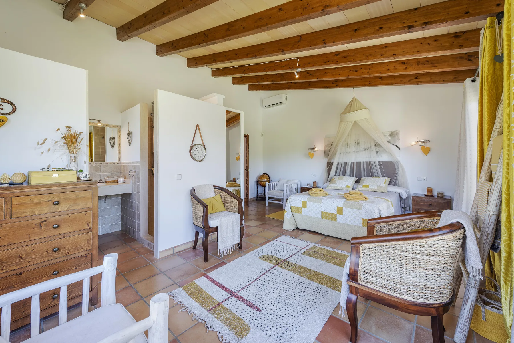 Dormitorio con cama con dosel, asientos y vigas expuestas en el techo.
