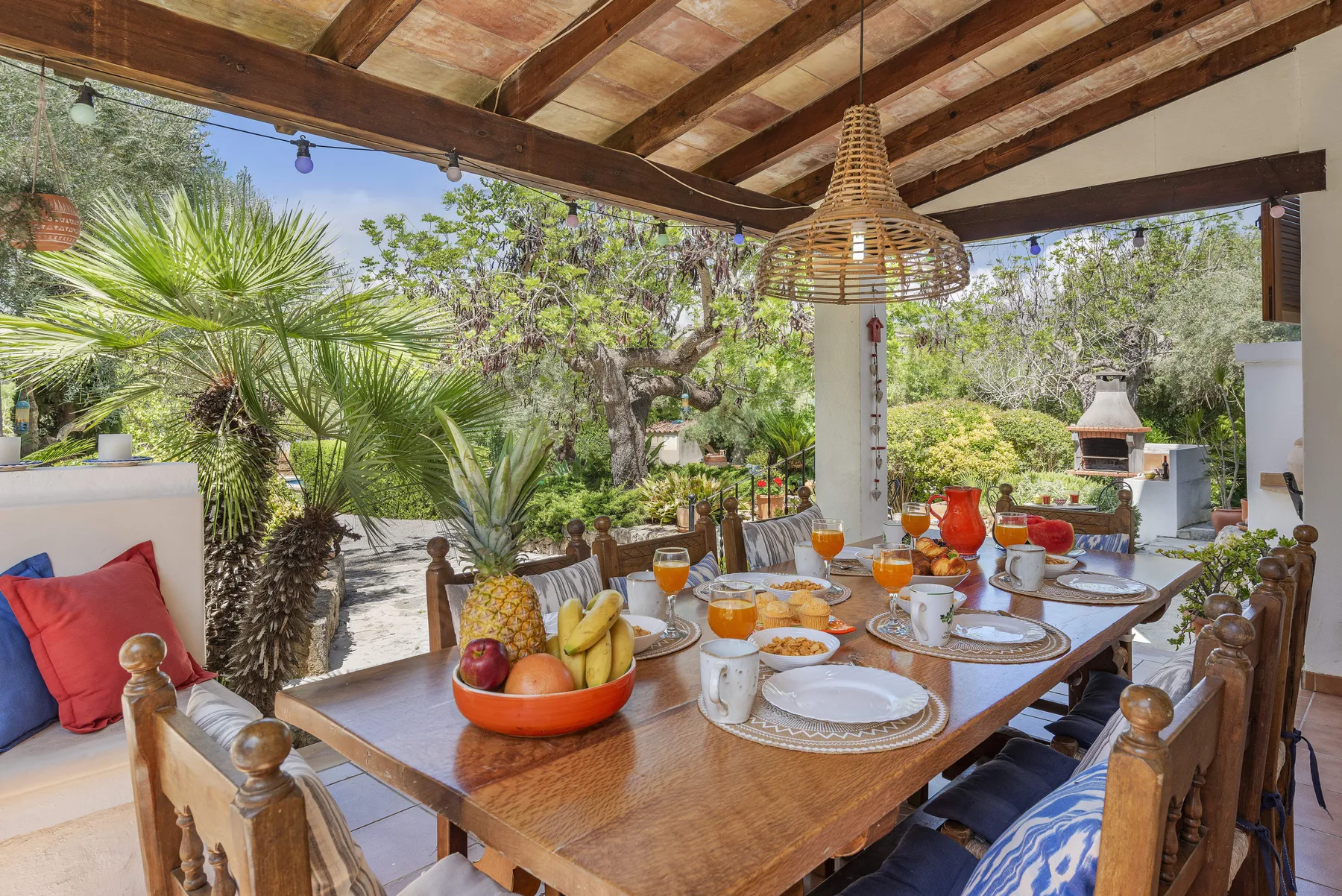 Una zona de comedor exterior cubierta con una larga mesa de madera rodeada de plantas.