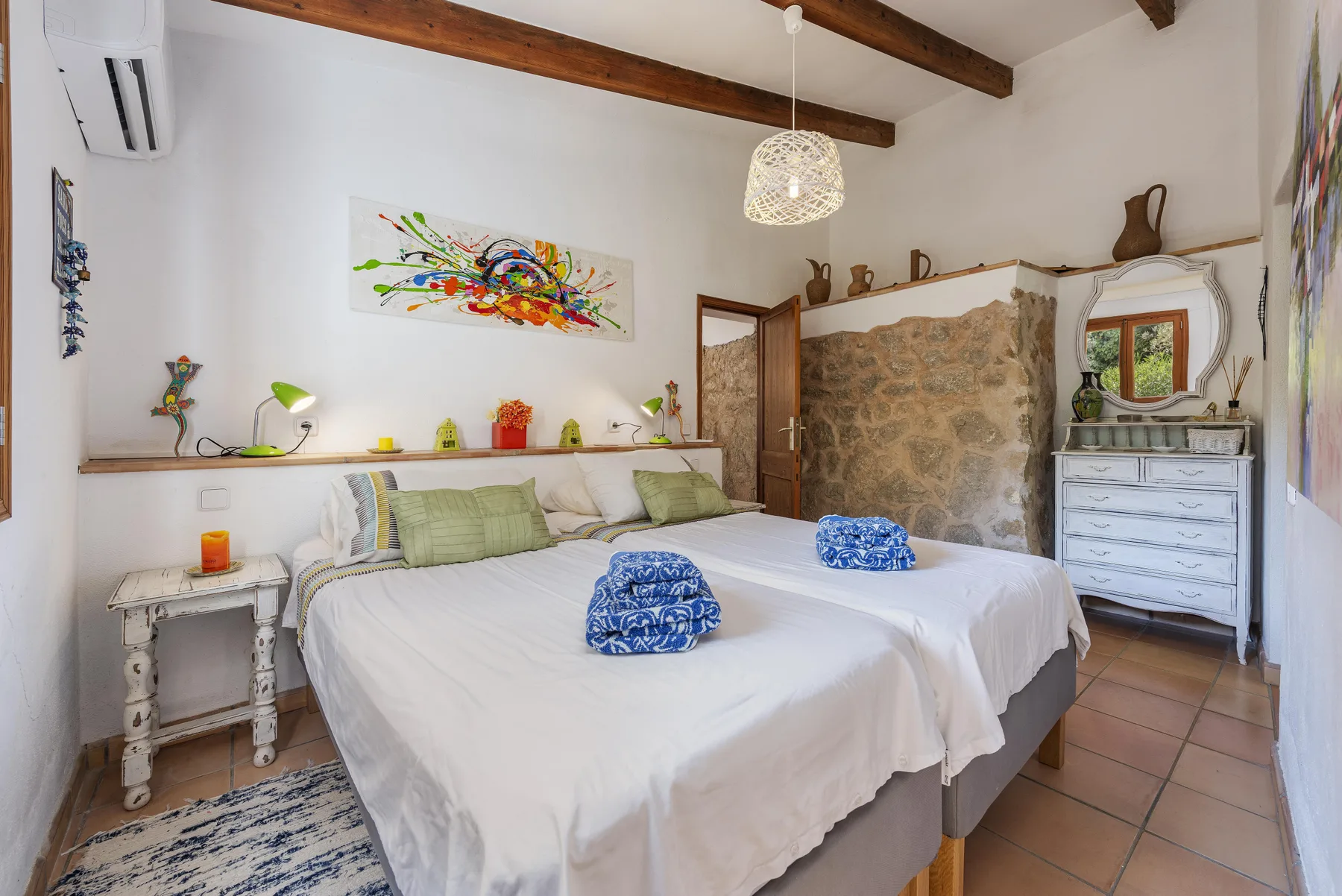 Un dormitorio con dos camas, arte colorido y una pared de piedra.
