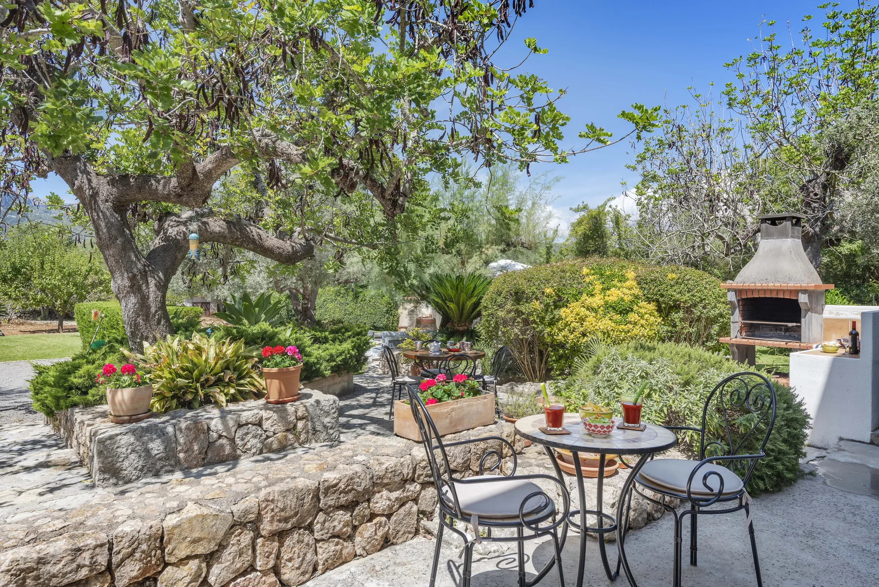 Un patio de jardín con asientos al aire libre, flores en macetas y una barbacoa de piedra.
