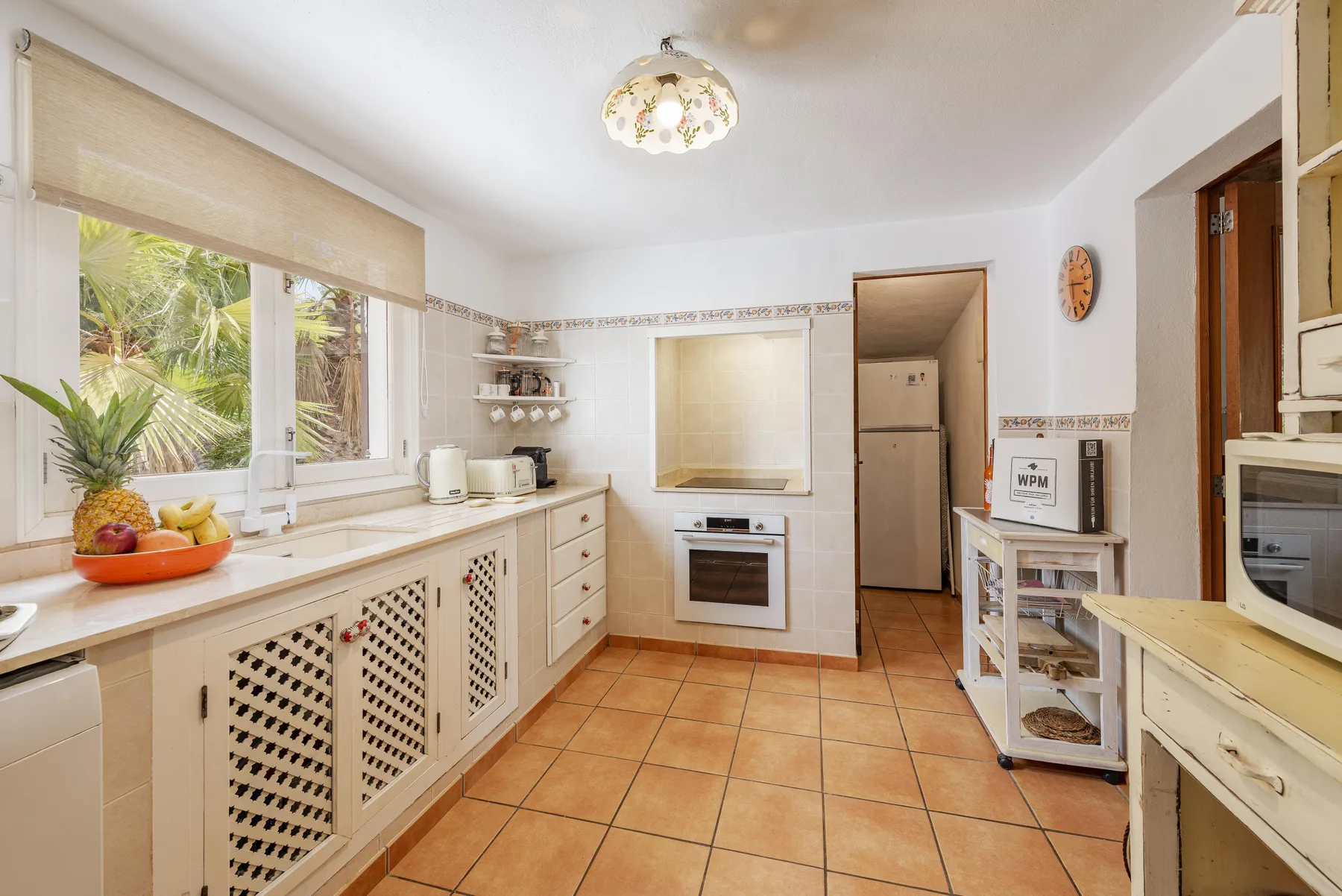 Una cocina luminosa con suelo de baldosas, armarios blancos y una ventana con vista a la vegetación.