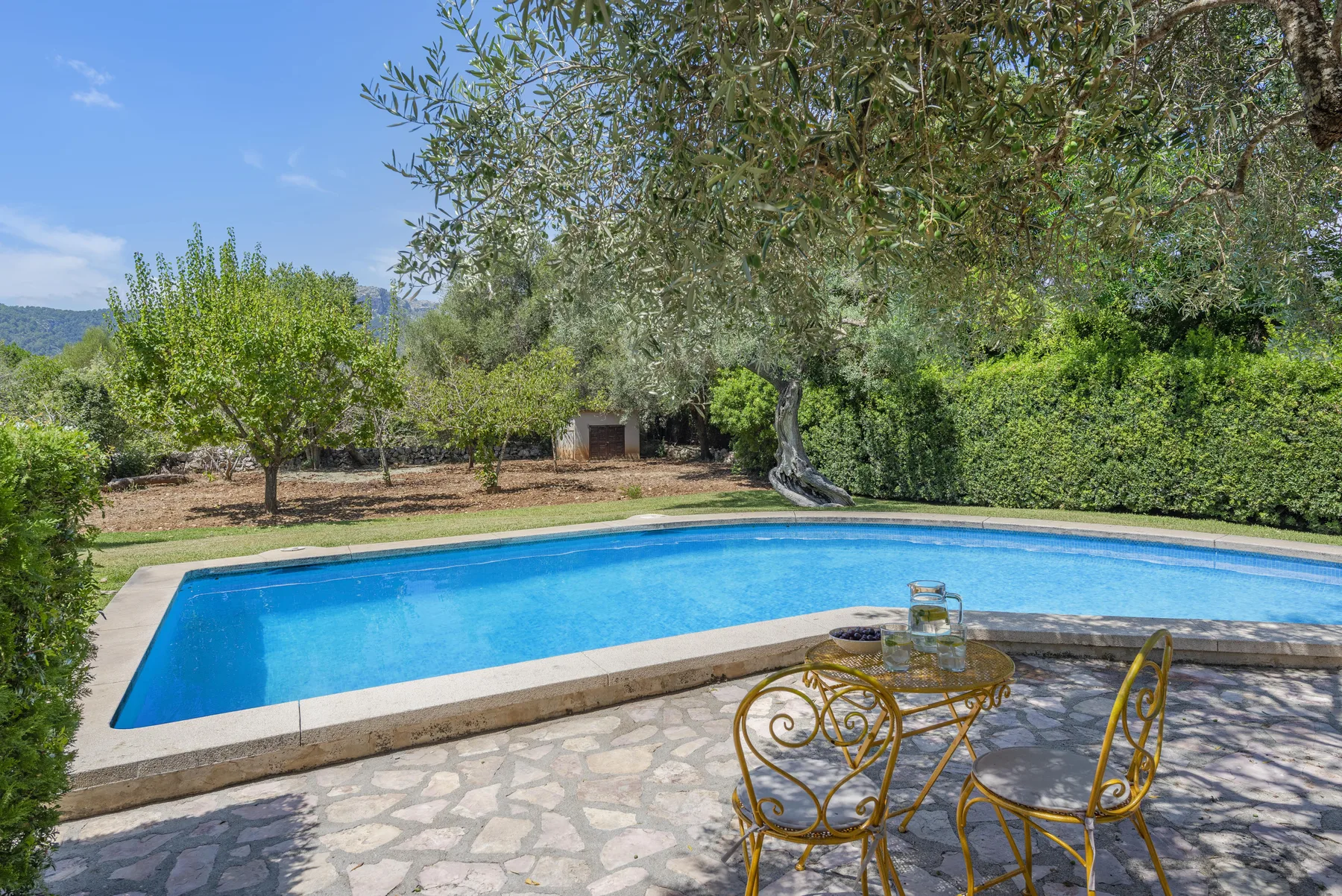 Una piscina exterior junto a un patio de piedra y asientos decorativos.