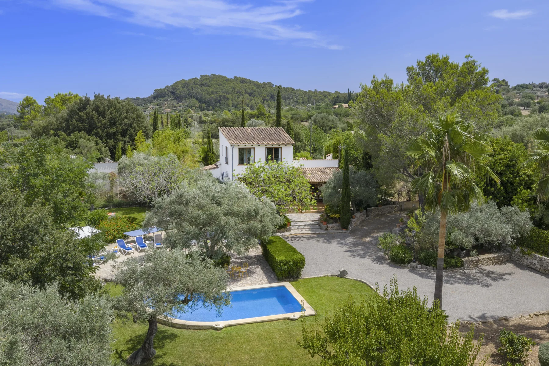 Una casa de campo y una piscina están rodeadas de árboles y jardines.