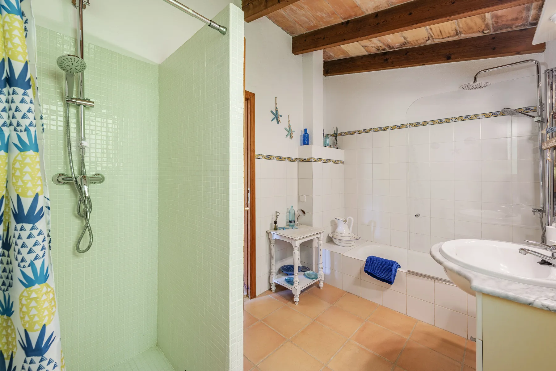 Un baño alicatado con ducha, lavabo y vigas de madera expuestas en el techo.
