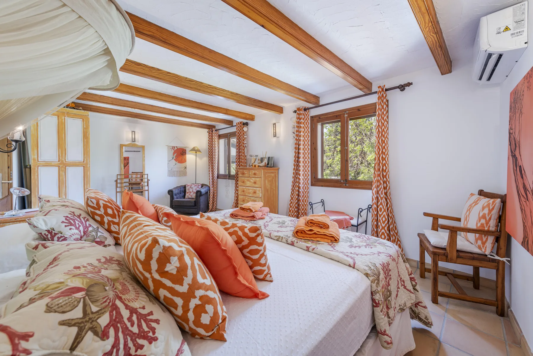 Un dormitorio con ropa de cama estampada, vigas de madera en el techo y una ventana con vistas a la vegetación.
