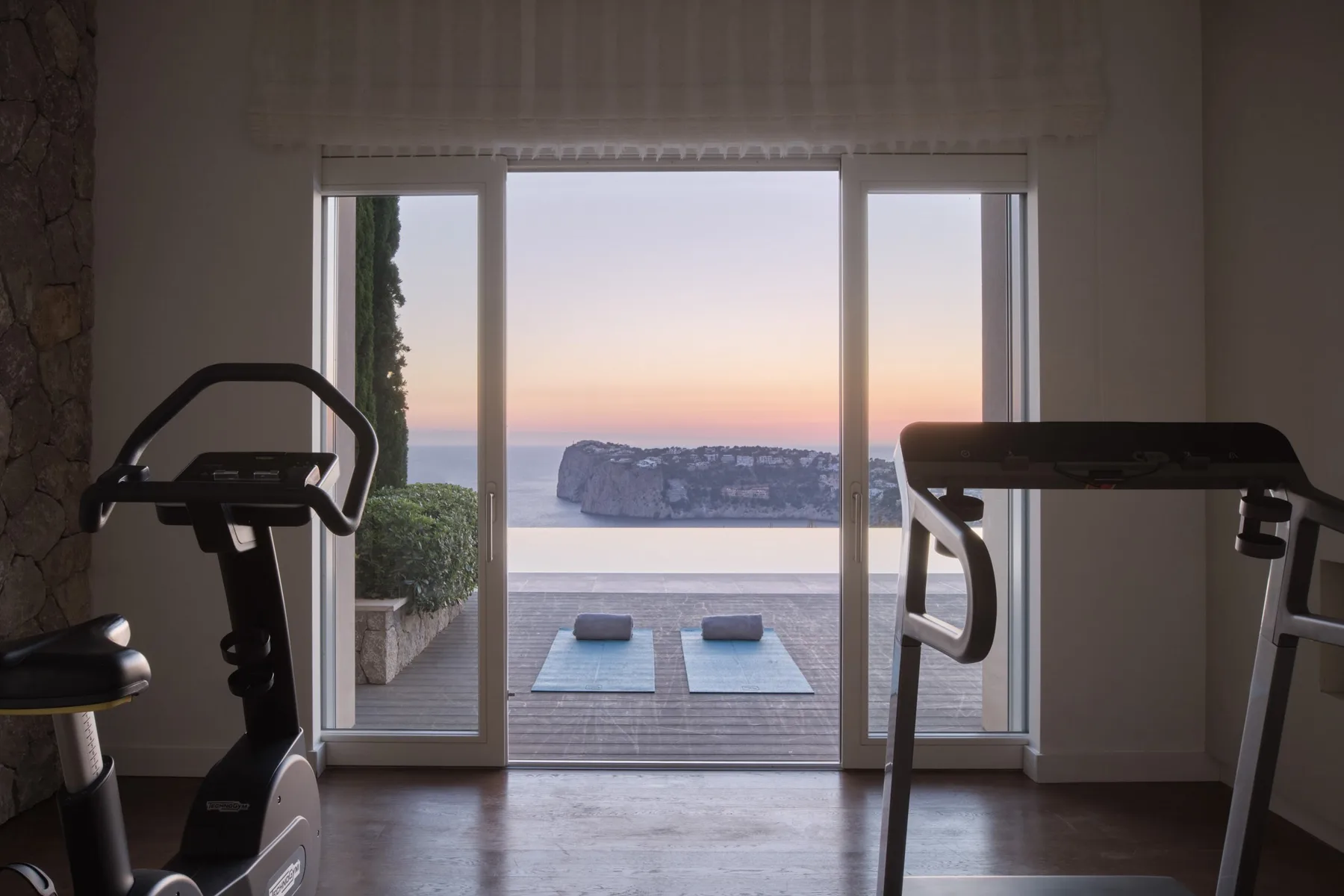 A workout area faces glass doors opening onto a terrace with ocean views.