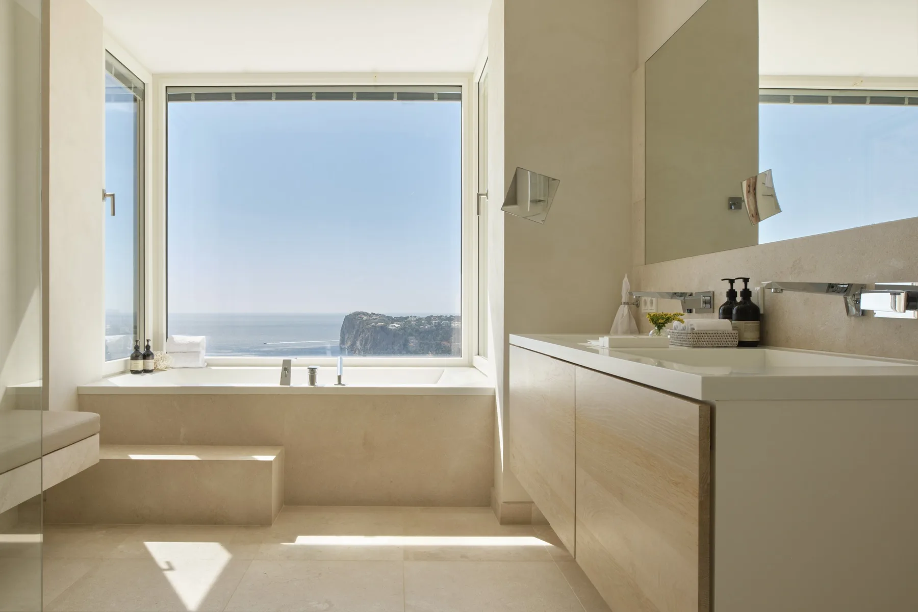 A bright bathroom with a wide window overlooking the sea.